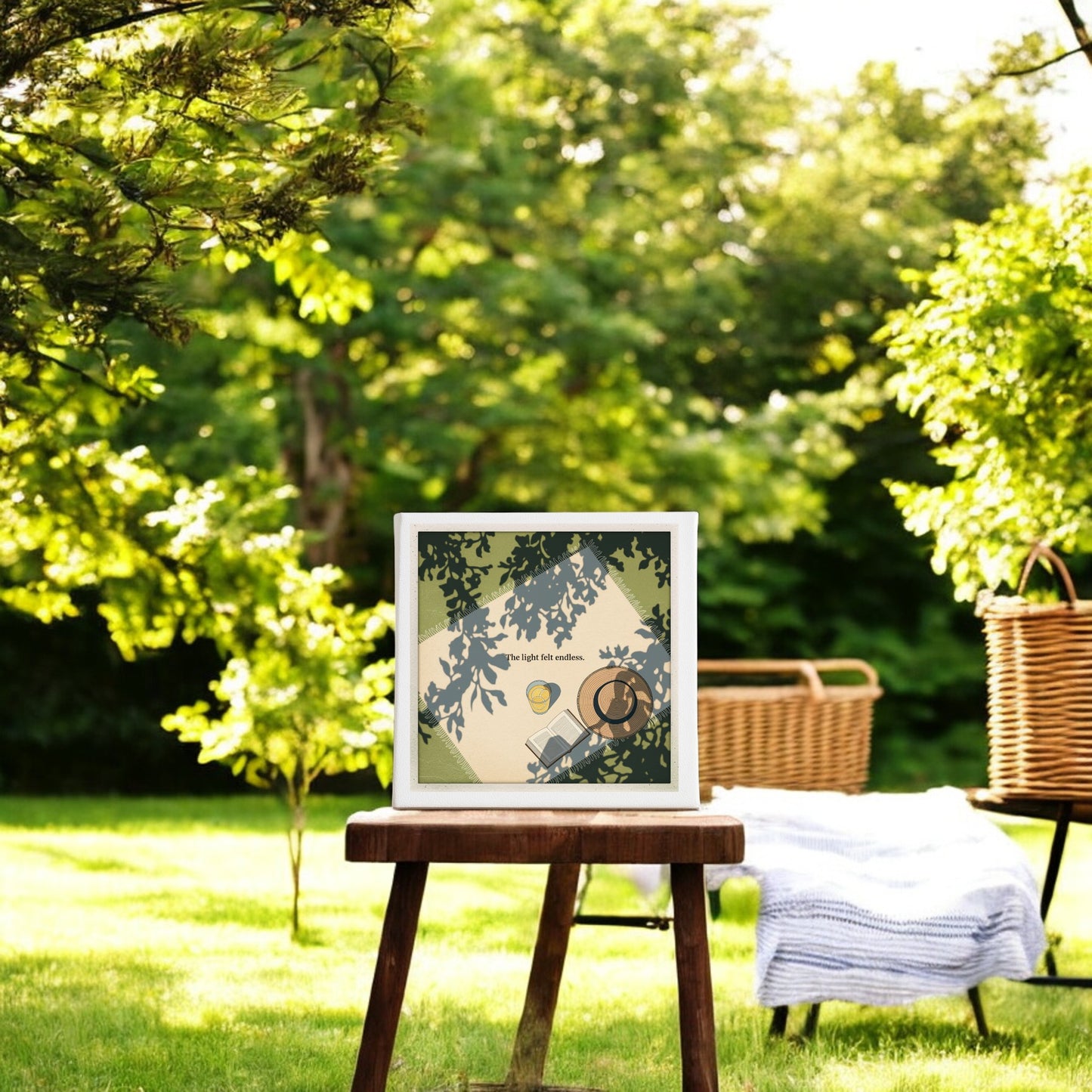 The Light Felt Endless Canvas – Summer Stillness Art by Mirabilia Boutique is displayed on a wooden stool in a sunlit garden, with green trees, grass, a woven basket, and striped blanket creating a calm, slow living vibe.