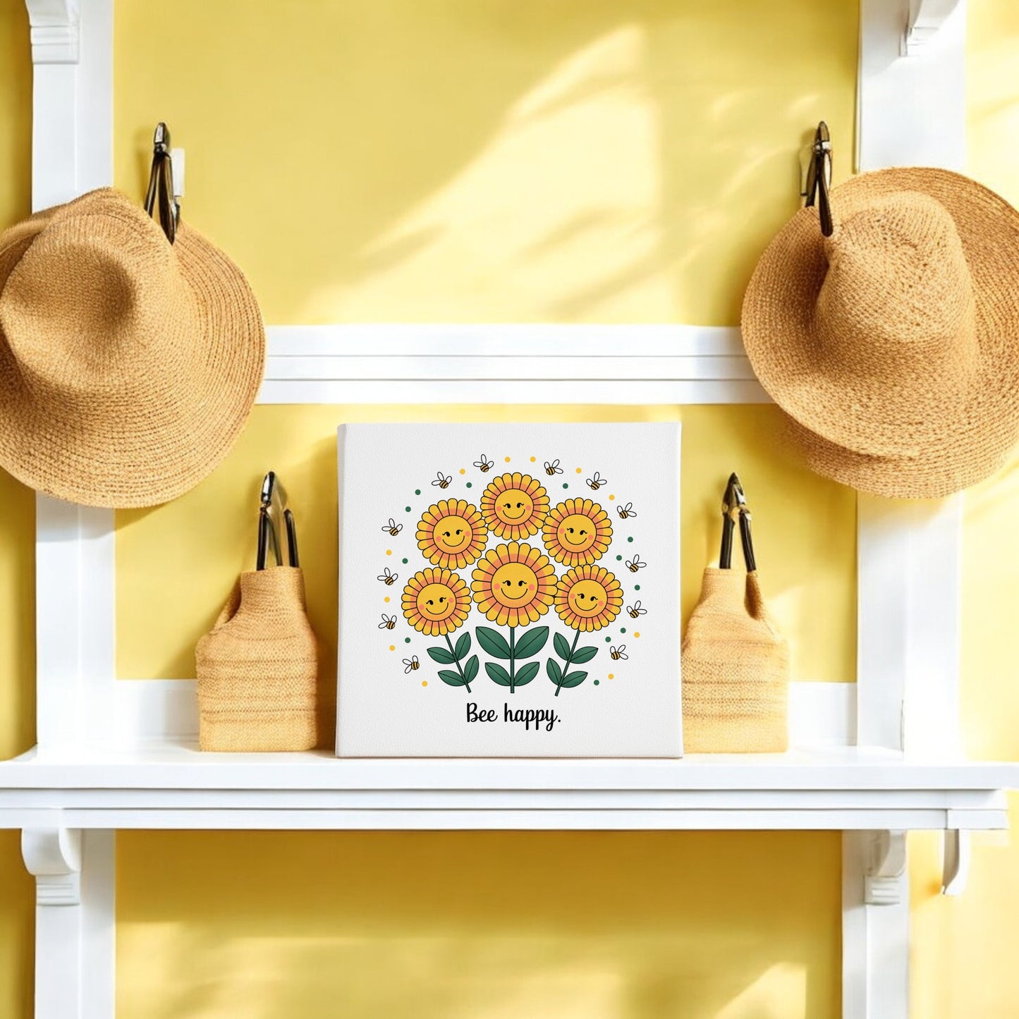 A white shelf against a yellow wall displays two straw hats, two straw bags, and Mirabilia Boutique’s Bee Happy Canvas—smiling sunflowers with “Be happy”—bringing cheerful summer decor into your home.