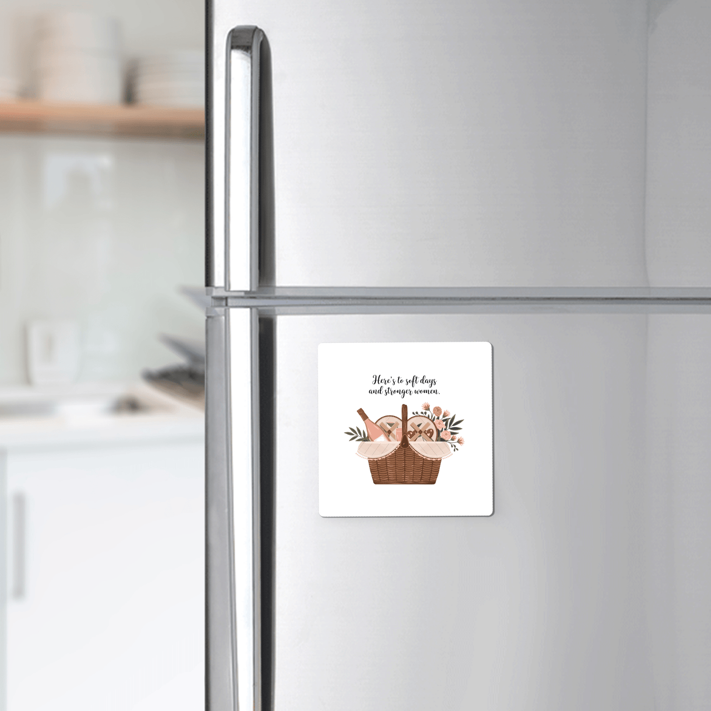 The Soft Days Strong Women Magnet by Mirabilia Boutique, featuring a basket of bread, cheese, and flowers, is displayed on a stainless steel fridge—a modern kitchen accent and a perfect feminine empowerment gift.