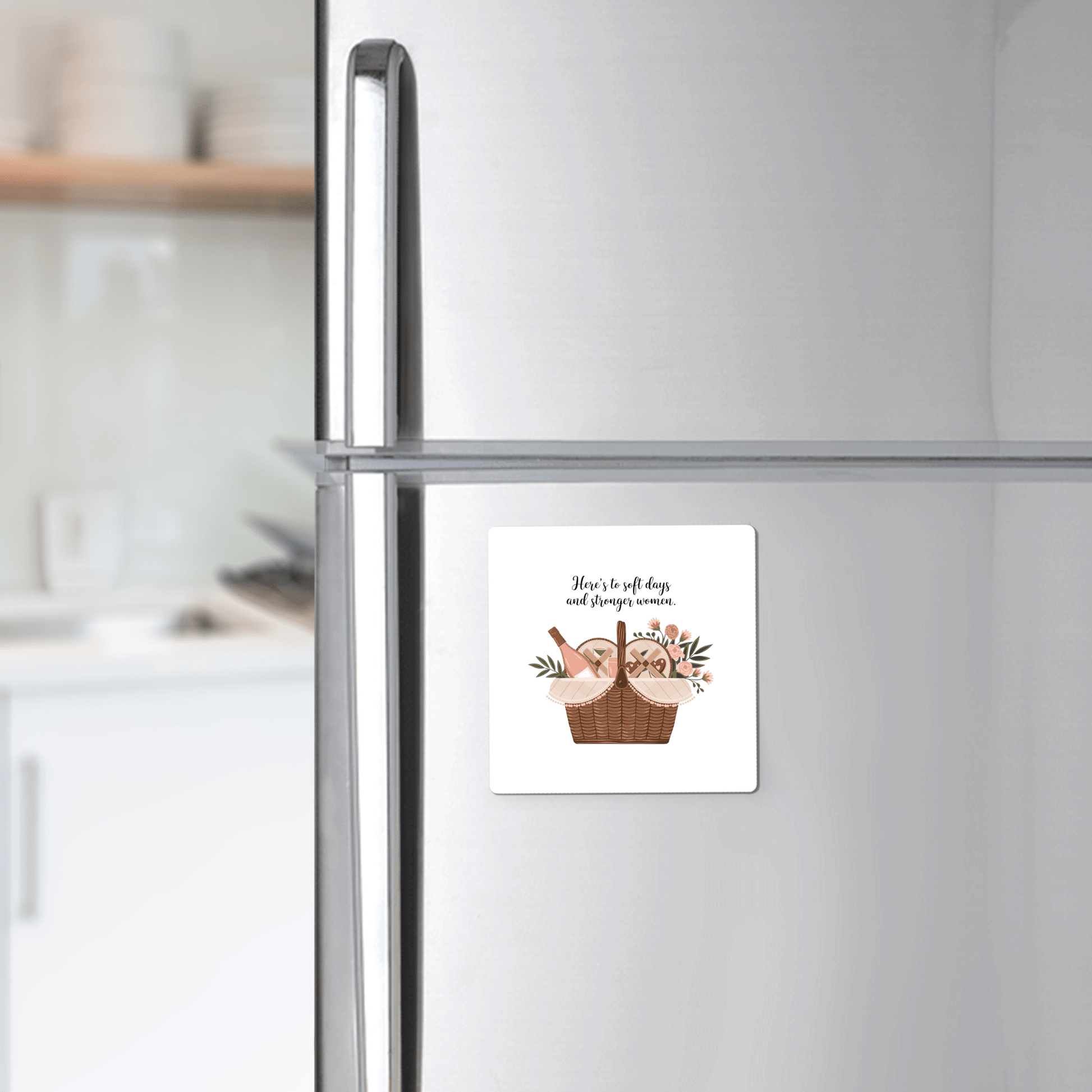 The Soft Days Strong Women Magnet by Mirabilia Boutique, featuring a basket of bread, cheese, and flowers, is displayed on a stainless steel fridge—a modern kitchen accent and a perfect feminine empowerment gift.