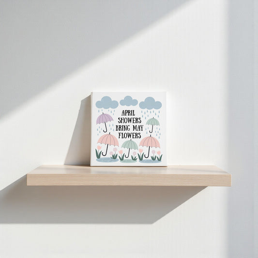 The April Showers Bring May Flowers Canvas Art by Mirabilia Boutique features pastel umbrellas and blooms under clouds, with its title at the center—charming spring wall decor ideal for nurseries or shelves.