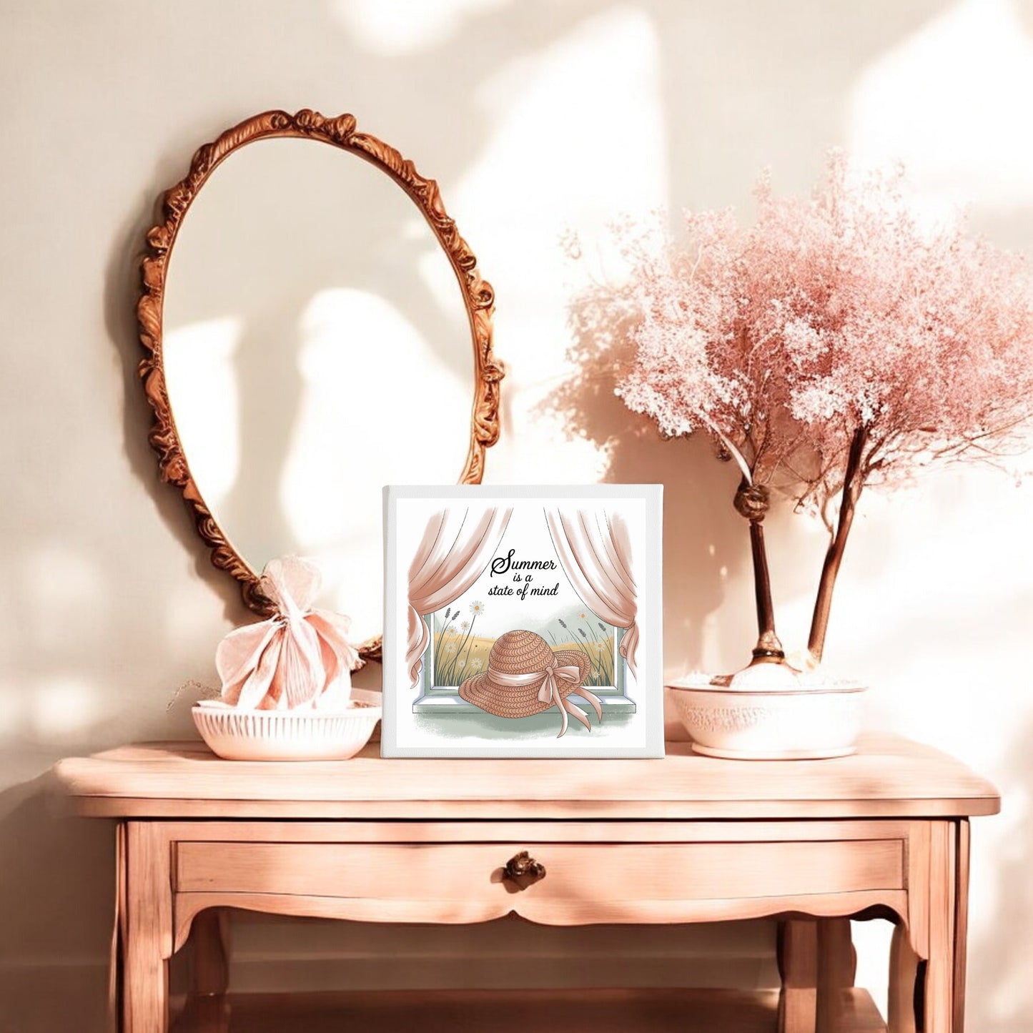 A wooden vanity table with a round ornate mirror, Mirabilia Boutique’s "Summer Is a State of Mind Canvas – Soft Cottagecore Art" framed beside it, a soft pink pouch, and pastel pink flowers in sunlight.