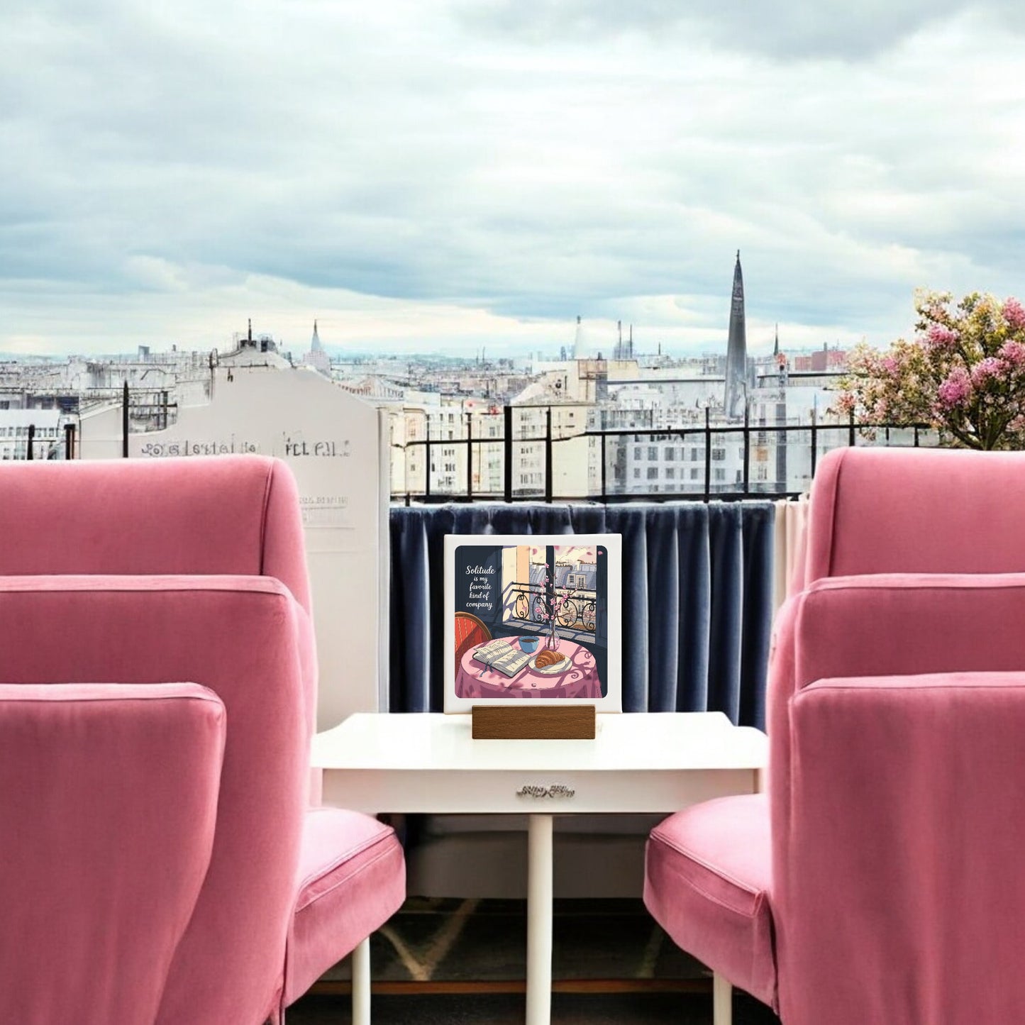 The Solitude Mini Sign – Parisian Morning Still Life by Mirabilia Boutique adds Parisian charm, featuring pink armchairs, a white table with an upright book, and city views—ideal balcony décor for a cozy retreat.