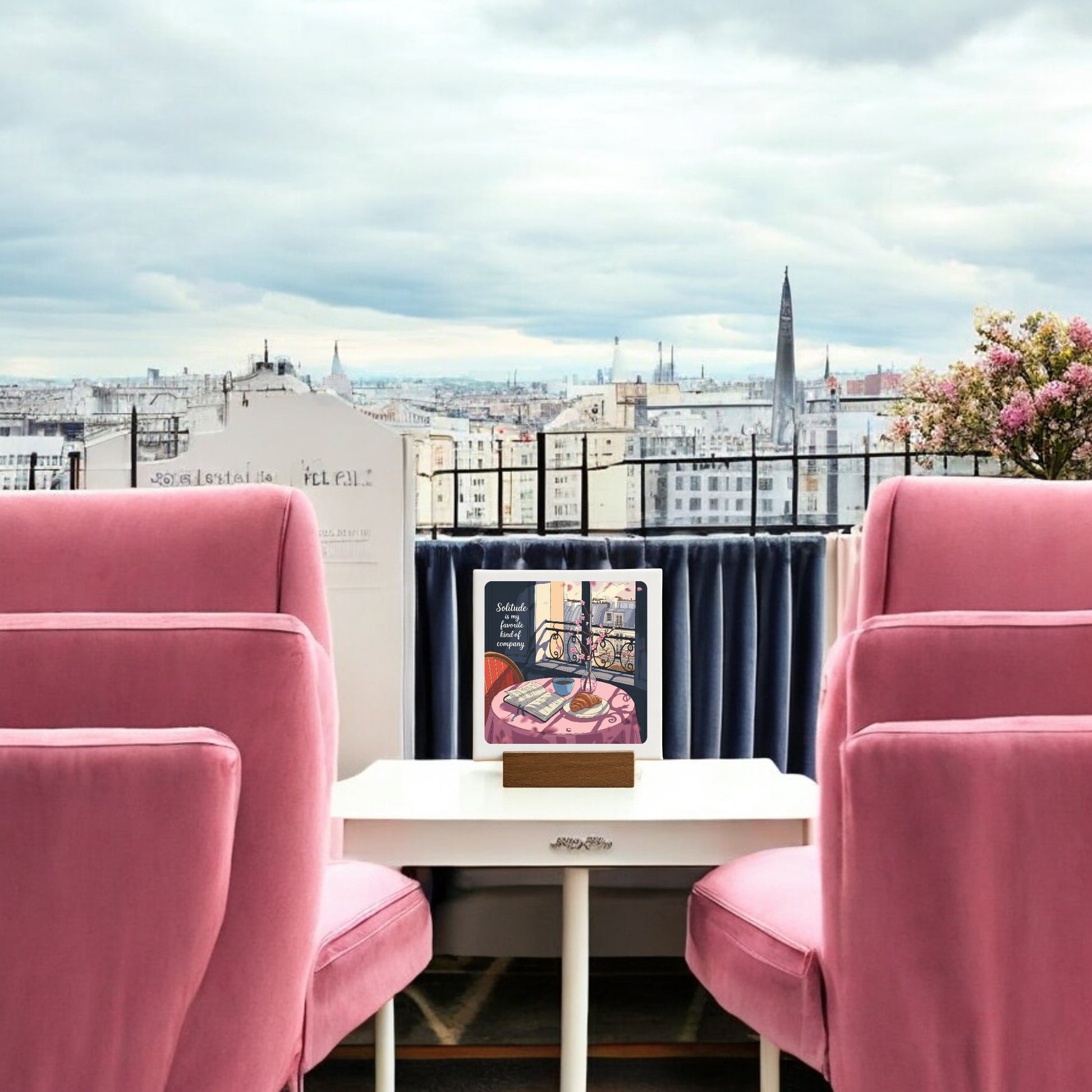 The Solitude Mini Sign – Parisian Morning Still Life by Mirabilia Boutique adds Parisian charm, featuring pink armchairs, a white table with an upright book, and city views—ideal balcony décor for a cozy retreat.