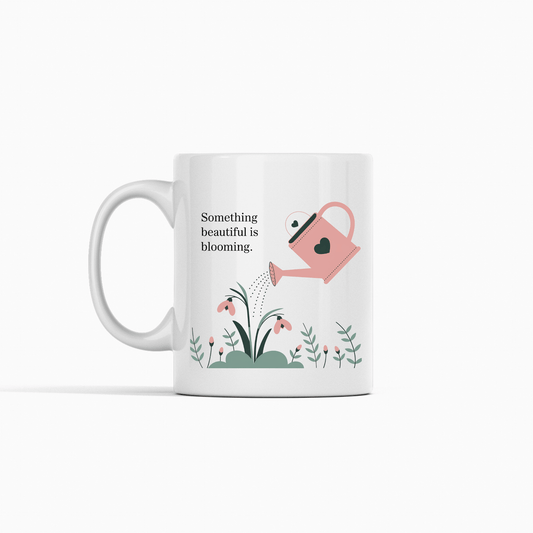 The Something Beautiful Is Blooming Mug by Mirabilia Boutique features a pink watering can watering flowers and the phrase "Something beautiful is blooming"—a perfect growth and positivity gift for daily inspiration.