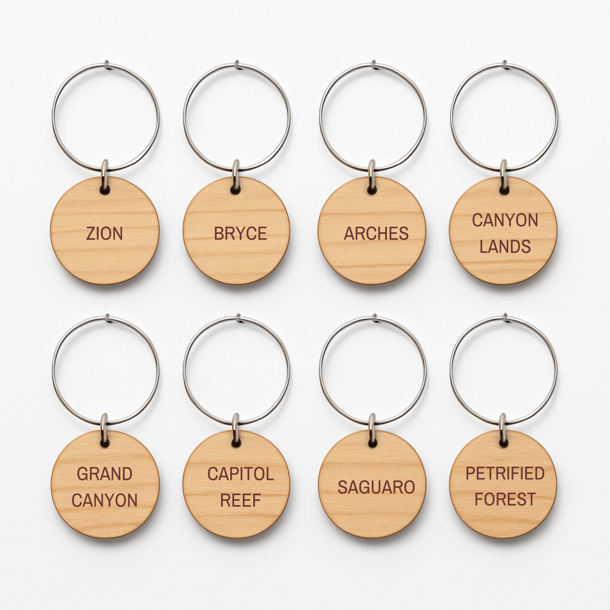 The Southwest National Park Wine Charms Set by Mirabilia Boutique includes eight round wooden keychains with metal rings, each engraved with a park name—an ideal rustic gift for adventurers and national park lovers.
