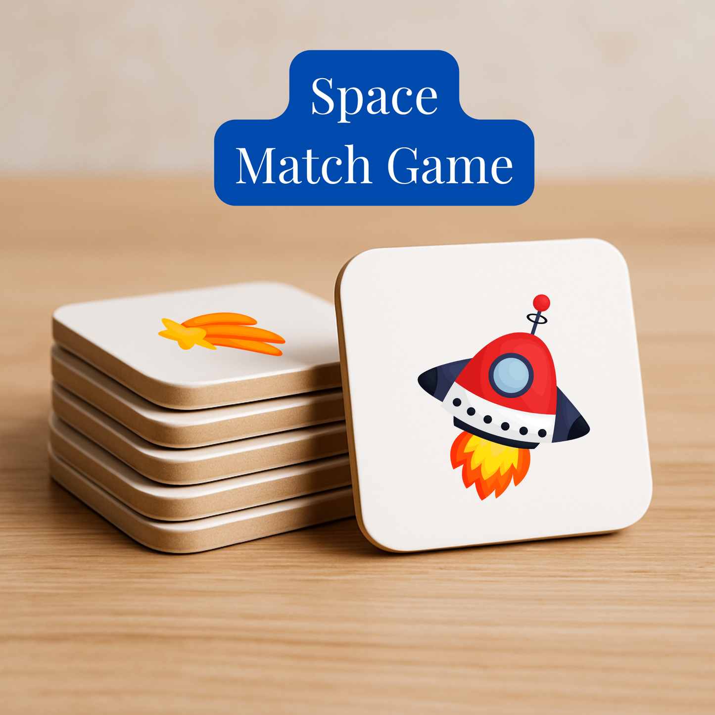 A stack of square cards from Mirabilia Boutique’s Space Match Game | Kids Memory Game (15 Matching Pairs) sits on wood; the top card shows a cartoon rocket, the next a shooting star, hinting at its fun space-themed memory gameplay.