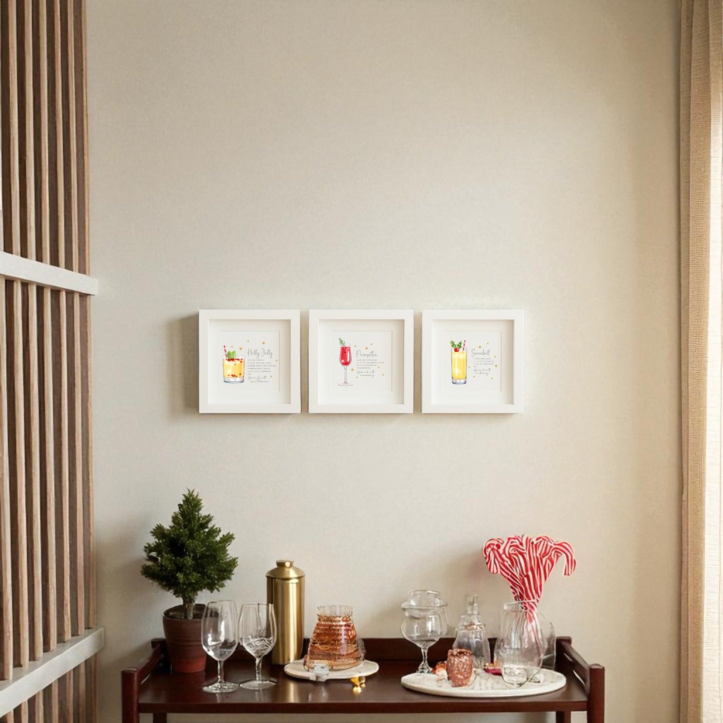 A small bar cart with glasses, a shaker, candy canes, and a mini tree sits beneath Mirabilia Boutique's "Sparkly Holiday Cocktails" 5x5 Shadowbox Trio festive bar art on a beige wall in a cozy, well-lit room.