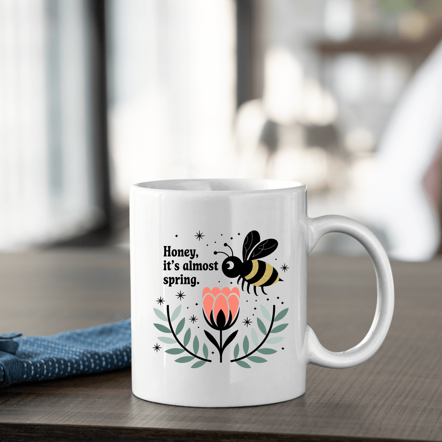The Mirabilia Boutique Spring Bee Mug features a cute bee, pink flower, green leaves, and “Honey, It’s Almost Spring” text—perfect for coffee. This charming mug adds a touch of spring to any table.
