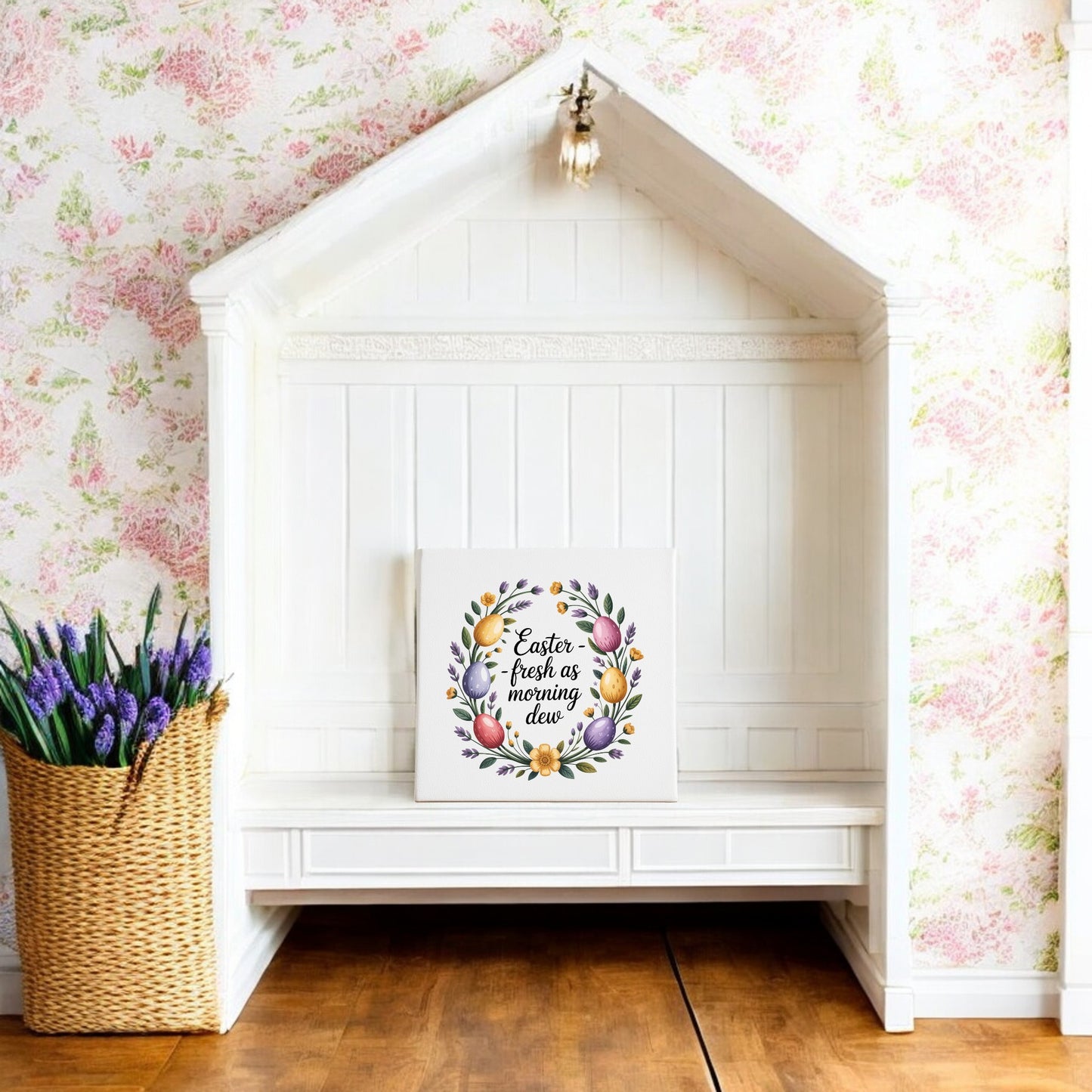 A white nook with a peaked roof displays the Mirabilia Boutique "Easter Morning Dew Floral Egg Canvas Art." A woven basket of purple flowers sits on the wooden floor, and pink floral wallpaper decorates the wall.