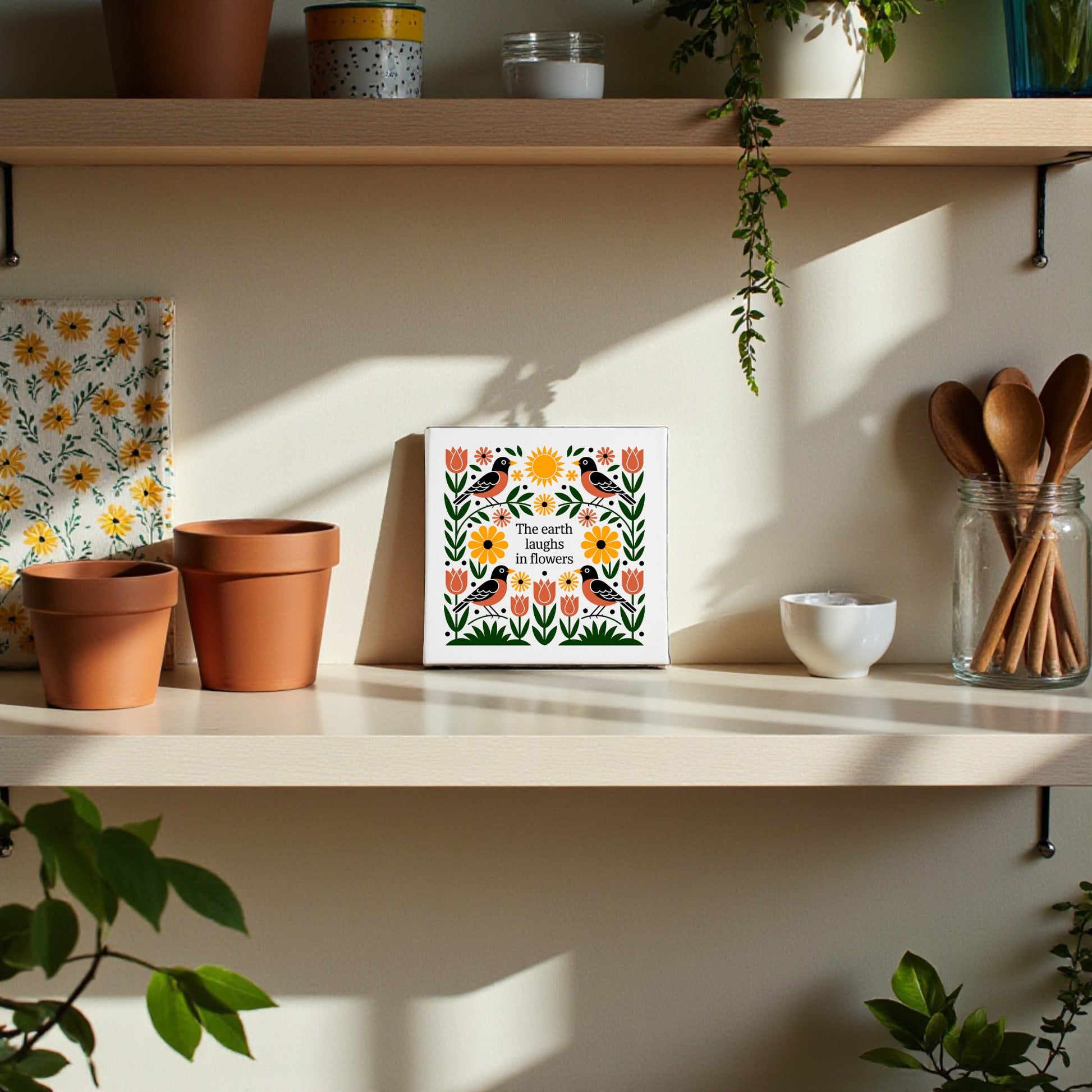 A sunlit kitchen shelf with potted plants, wooden utensils, a floral cloth, and the Mirabilia Boutique "The Earth Laughs in Flowers" Canvas Wall Art, surrounded by colorful wildflower artwork and folk art decor.
