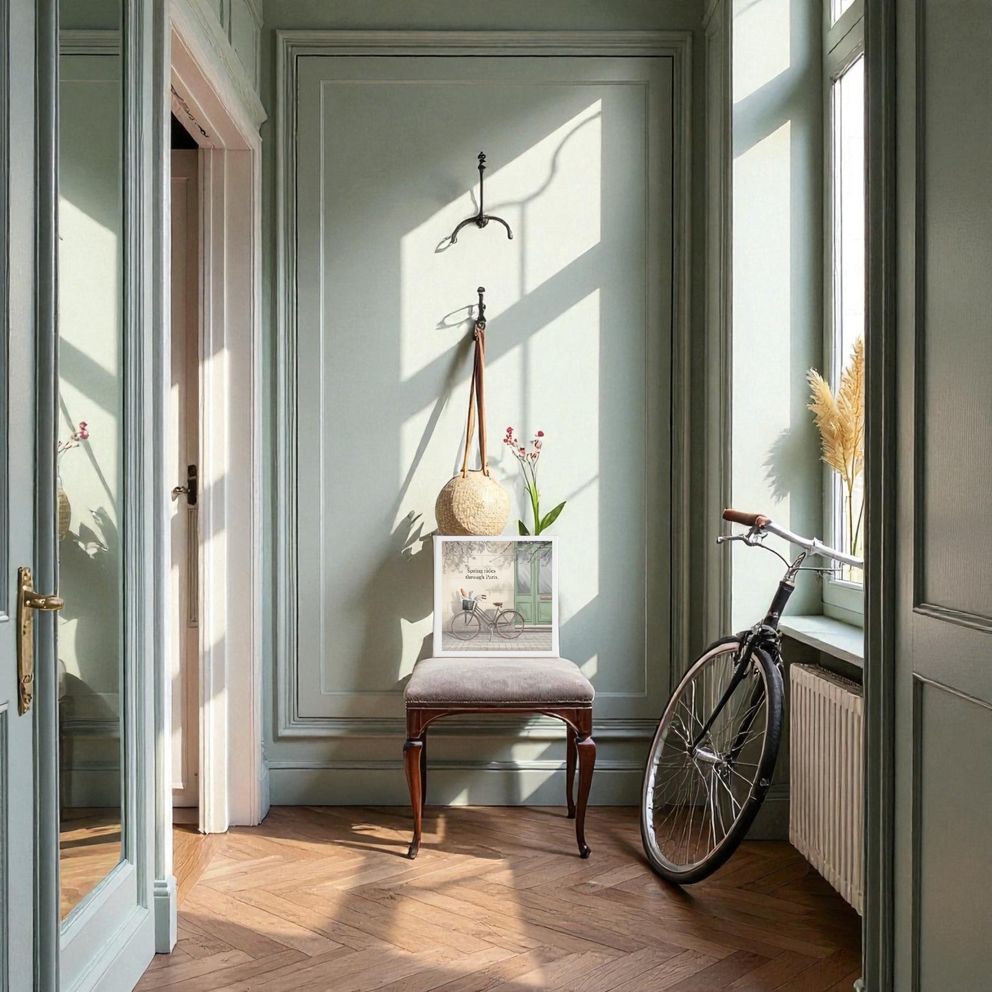 A sunlit hallway with sage green walls, wooden herringbone floors, and a vintage chair with flowers is adorned by Mirabilia Boutique's "Spring Rides Through Paris" canvas art. Sunlight streams in as a bicycle rests near the window, creating dreamy spring vibes.
