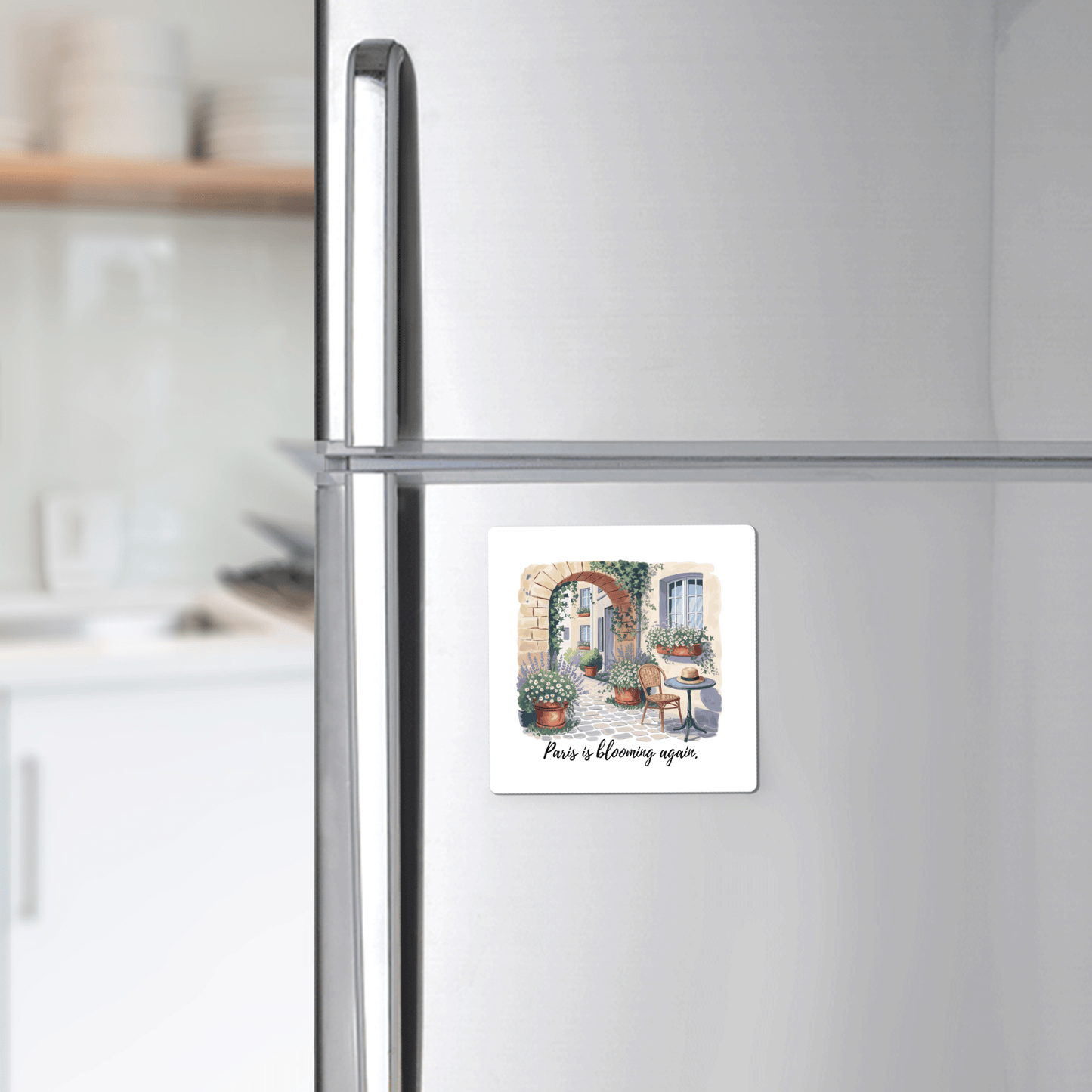 The Paris Is Blooming Again – Spring Courtyard Magnet by Mirabilia Boutique features a handcrafted design of a Parisian courtyard and the phrase "Paris is blooming again." A charming spring kitchen décor accent.