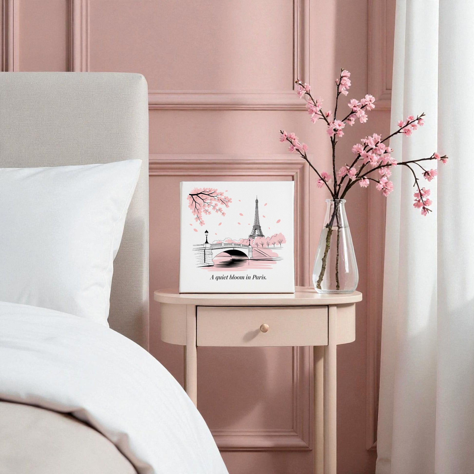 A small nightstand holds the Quiet Bloom in Paris Canvas – Cherry Blossom Spring Art by Mirabilia Boutique, styled with a cherry blossom vase, next to a bed with white bedding against a lovely pink paneled wall.