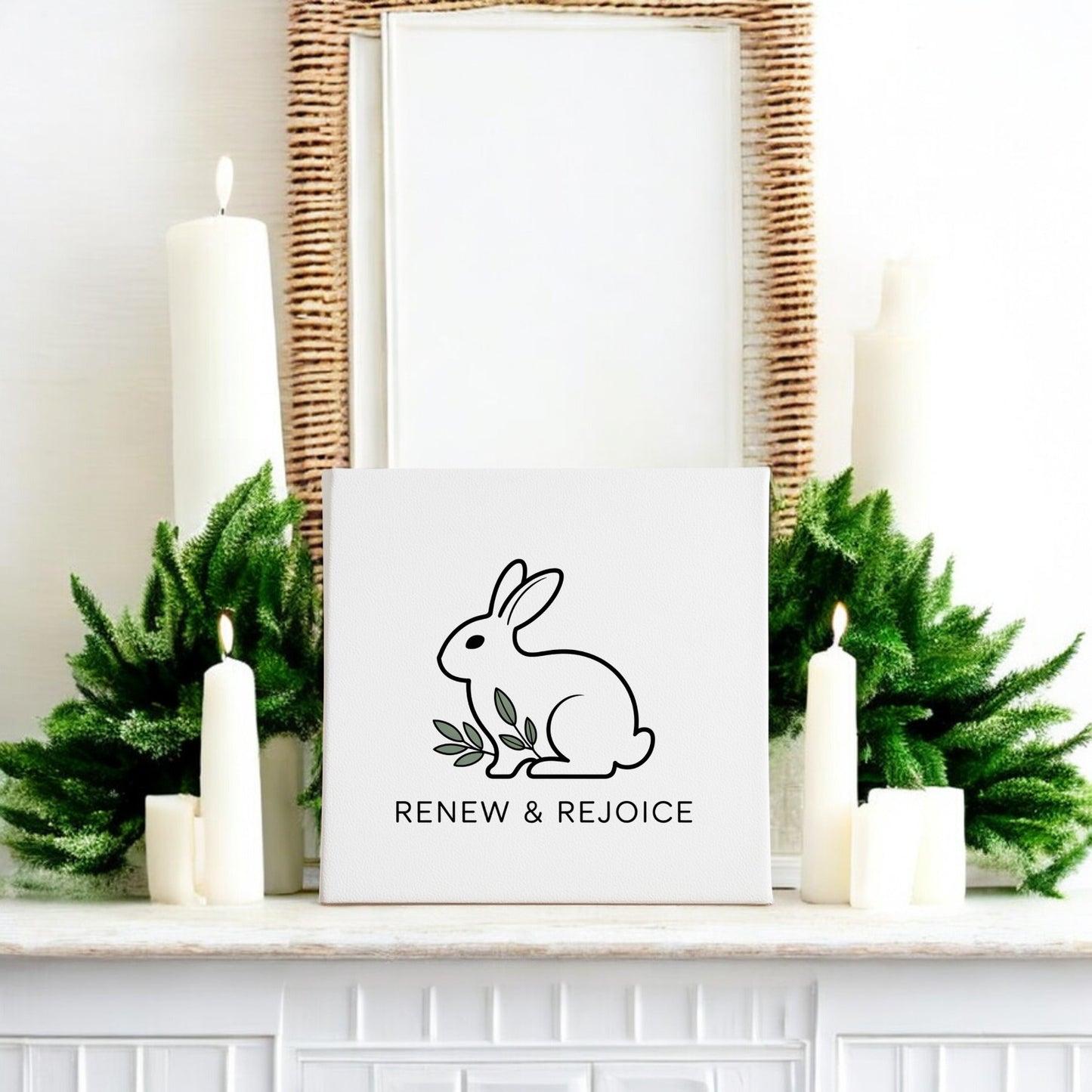 A white mantel with green foliage and white candles displays the Mirabilia Boutique Renew & Rejoice Bunny Canvas – 8x8 Spring Wall Art, featuring “RENEW & REJOICE.” A woven mirror above completes this charming Easter decor.