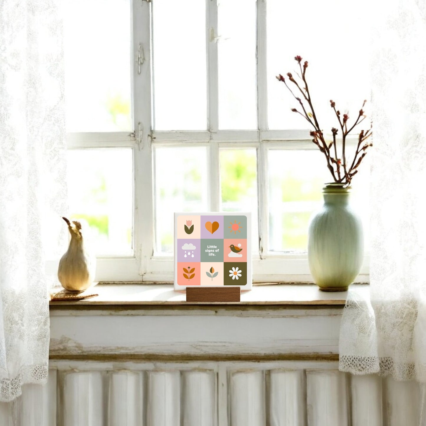 A bright windowsill with sheer white curtains features a green vase, yellow gourd, and the Mirabilia Boutique Little Signs of Life Mini Canvas Sign with Base. Soft light highlights these modern decor accents for an inspiring space.