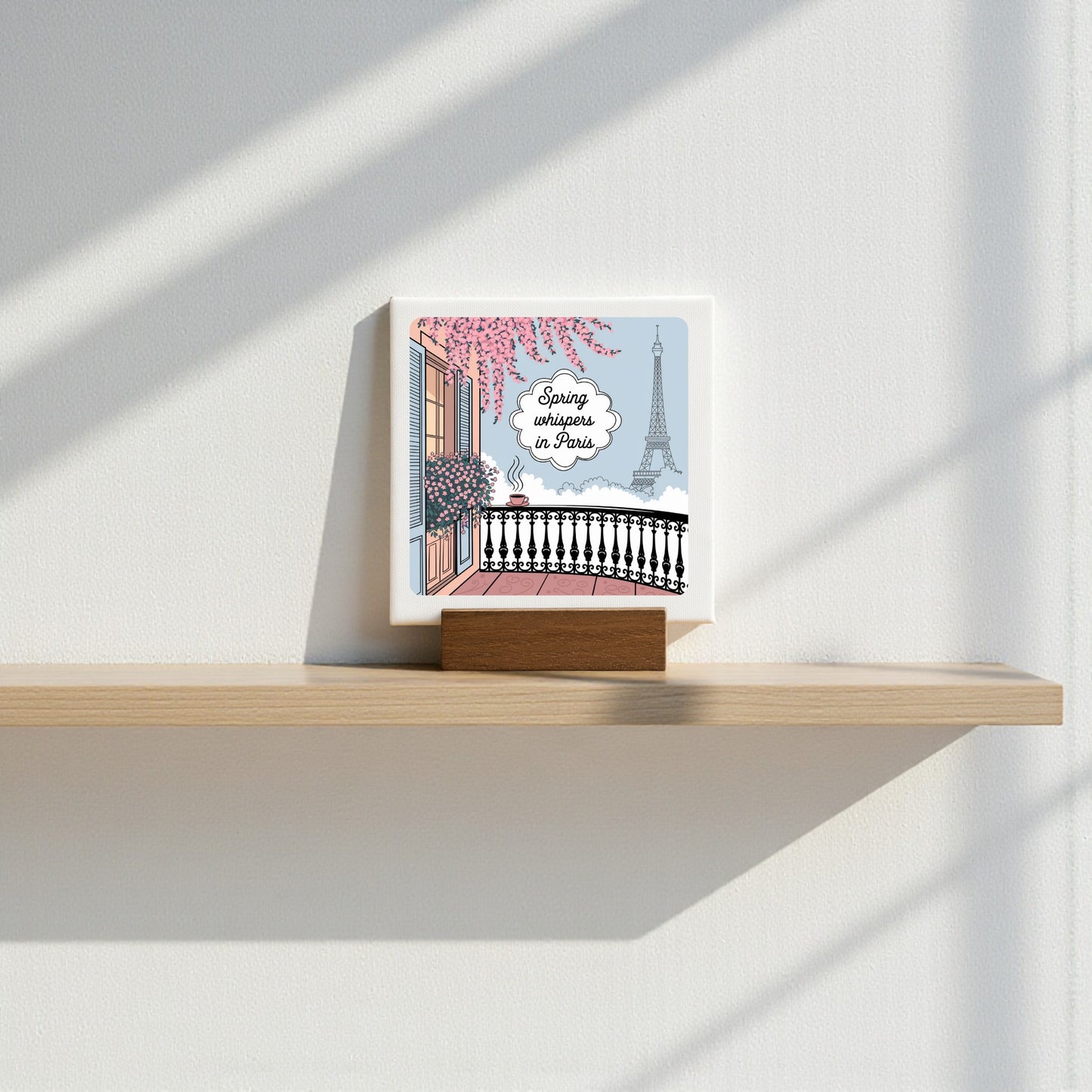 Mirabilia Boutique’s “Spring Whispers in Paris Mini Sign - Soft Paris Spring” features a handcrafted wood block with Parisian art—pink flowers, balcony, and the Eiffel Tower—and text: "Spring arrives in Paris." Sunlight casts delicate wall shadows.