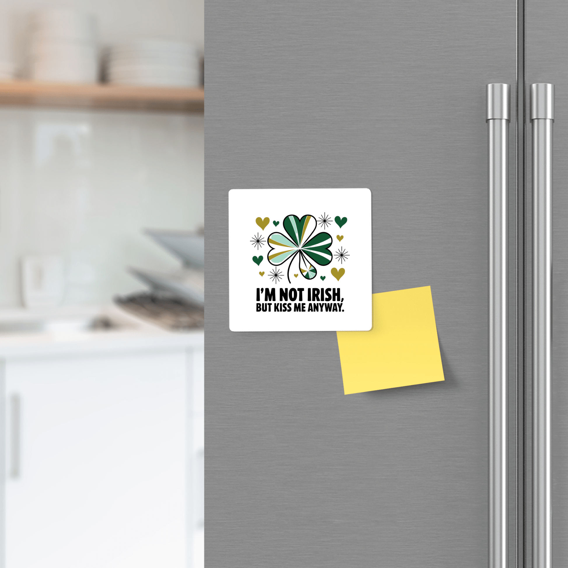A fridge displays the Mirabilia Boutique Kiss Me Anyway Funny St. Patrick’s Day Magnet with a green shamrock and playful text beside a blank yellow sticky note. A blurred background enhances this festive Irish party décor.