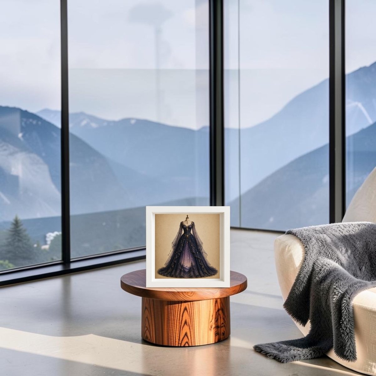 The “Moonrise Over Pines | Curated Couture Artwork” by Mirabilia Boutique, a collectible framed canvas featuring a woman in a celestial gown, is displayed on a wooden table in a modern room with floor-to-ceiling windows showcasing mountain views. A chair draped with a gray blanket sits nearby, elevating the decorative artistry of the space.