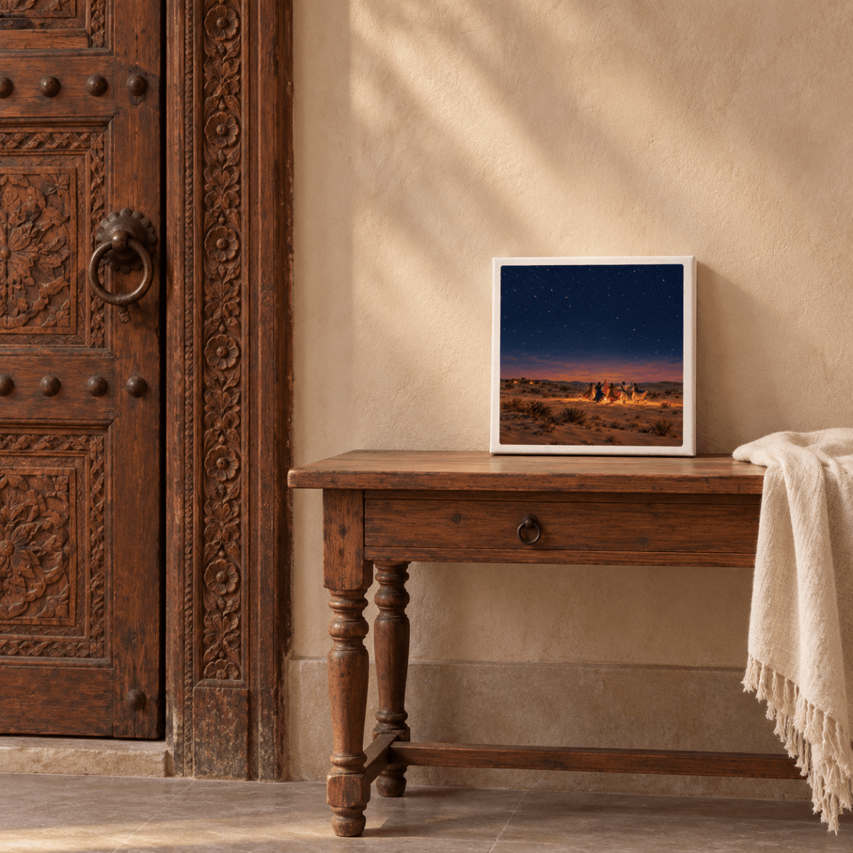 A square gallery-wrapped canvas print of The Night We Danced Canvas | Sand & Saffron, featuring a night landscape of figures around a campfire in the desert, resting on a wooden side table.