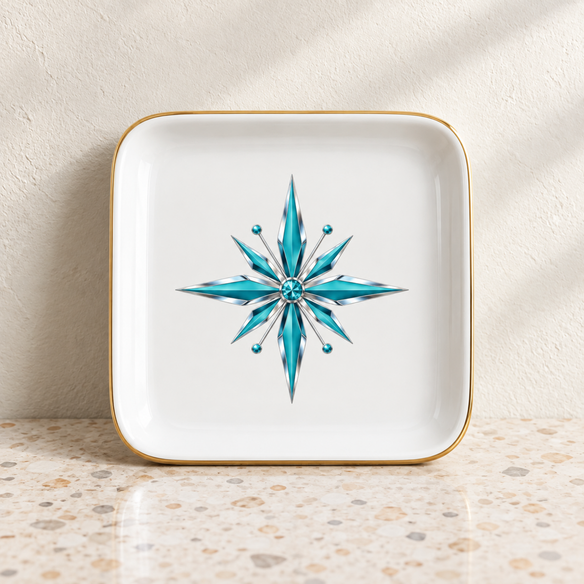 Starlite Starburst Ceramic Jewelry Tray square white ceramic tray with a gold rim and a turquoise starburst graphic in the center.