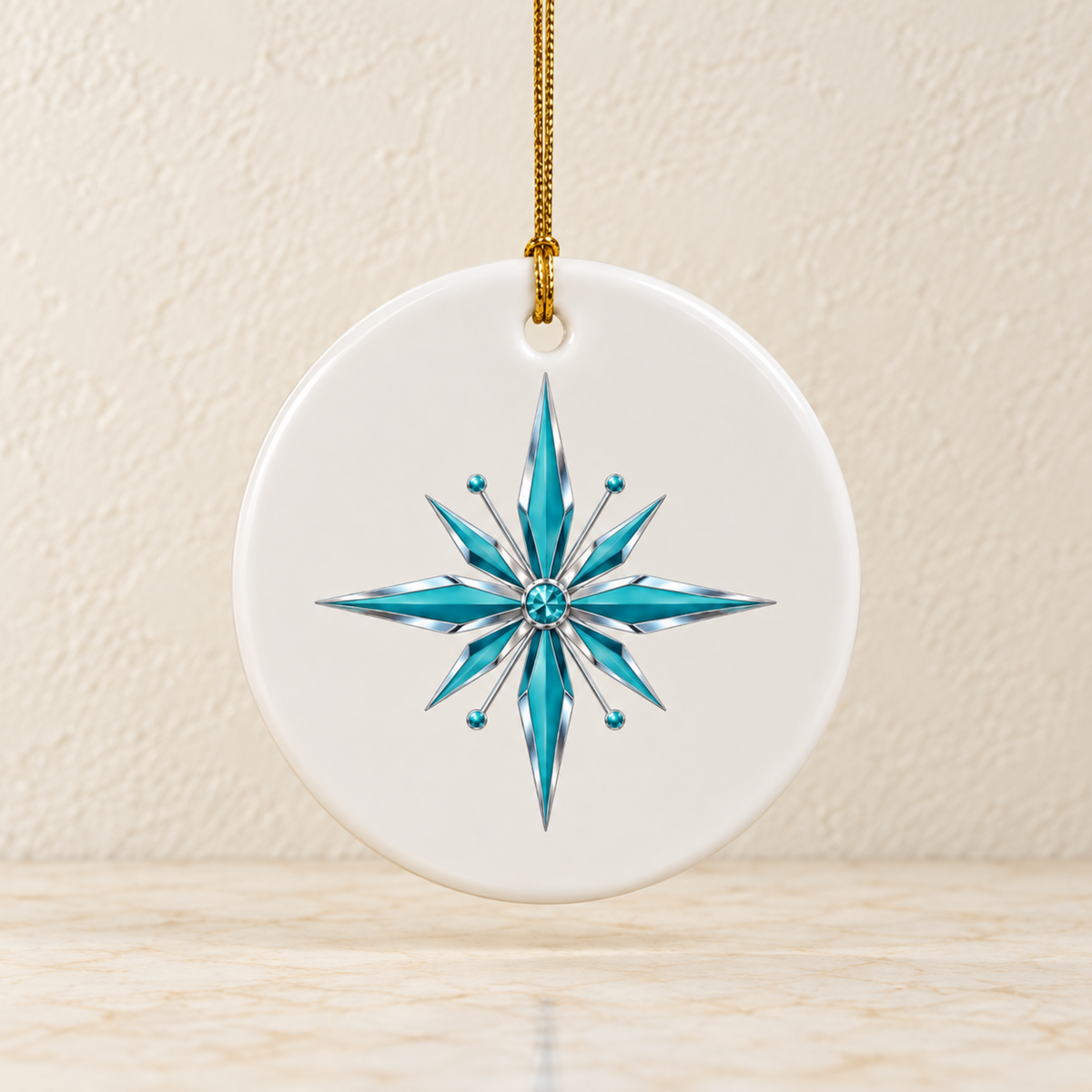 Starlite Starburst Ceramic Ornament | Chrome & Starlight: a round white ceramic Christmas ornament hanging by a gold string, featuring a stylized blue and silver starburst design in the center of this geometric holiday decoration.