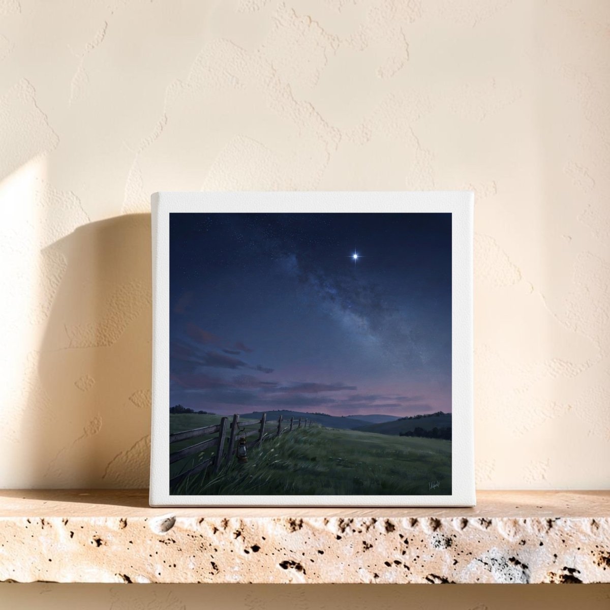 Bring tranquility to your home with the “Stay For The Stars 8x8 Canvas” from Mirabilia Boutique. This peaceful wall art showcases a luminous star shining over a cloudy night sky, grassy field, and rustic fence—perfectly complemented by display on a stone shelf against a textured beige wall.