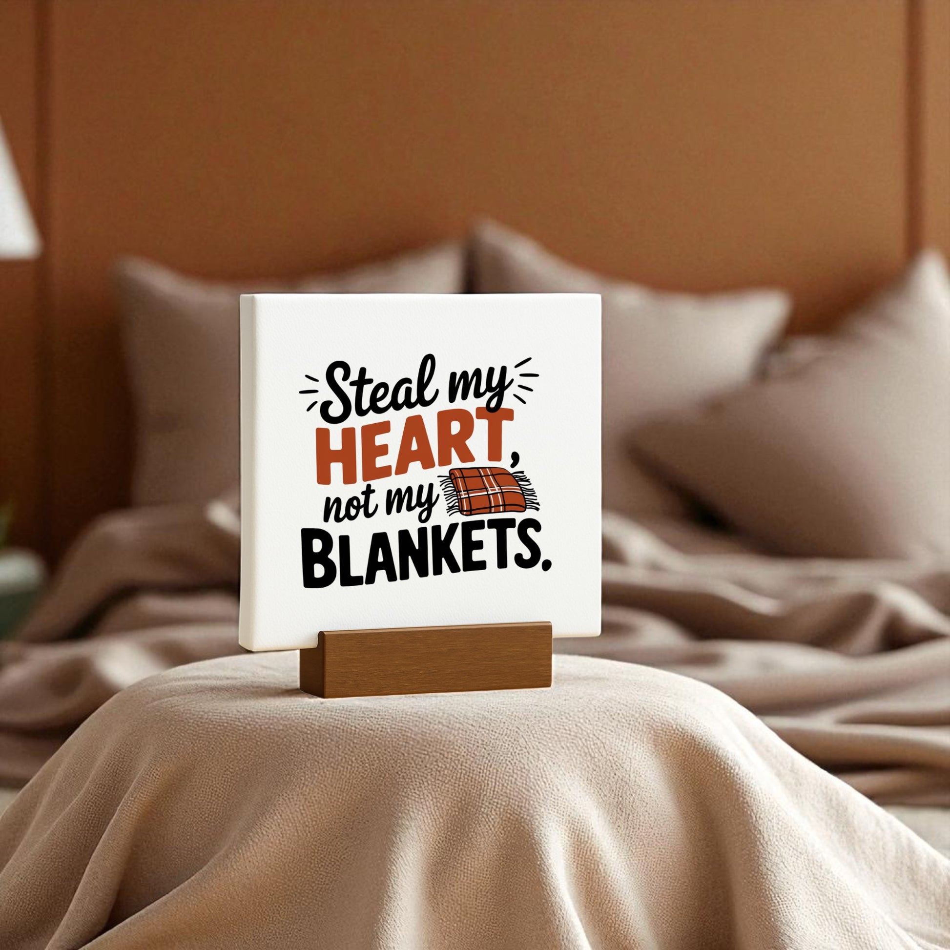 The Steal My Heart Mini Sign by Mirabilia Boutique, perfect for couples, sits on a neatly made bed with soft beige bedding and chic decor. Its witty "Steal my heart, not my blankets" message adds charm to any romantic bedroom.