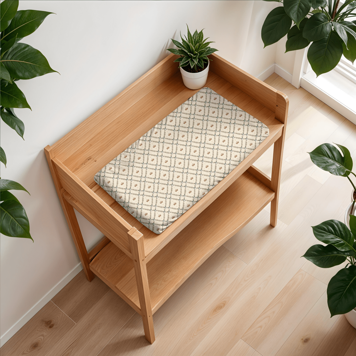A wooden changing table with the Storybook Trellis Changing Pad Cover from Mirabilia Boutique’s Moon & Moss Nursery collection, crafted from soft jersey knit polyester, topped with a potted plant and surrounded by green houseplants on a light wood floor near a window—an ideal finishing touch for your woodland nursery decor.