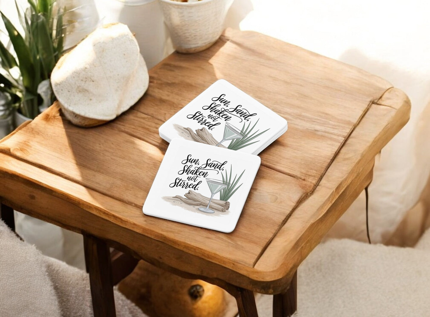 The Sun, Sand, Shaken Not Stirred Coaster Set by Mirabilia Boutique features two white coasters with palm leaf and driftwood designs plus the phrase "Sun. Sand. Shaded. Salted."—perfect for adding a coastal summer vibe to your bar cart.