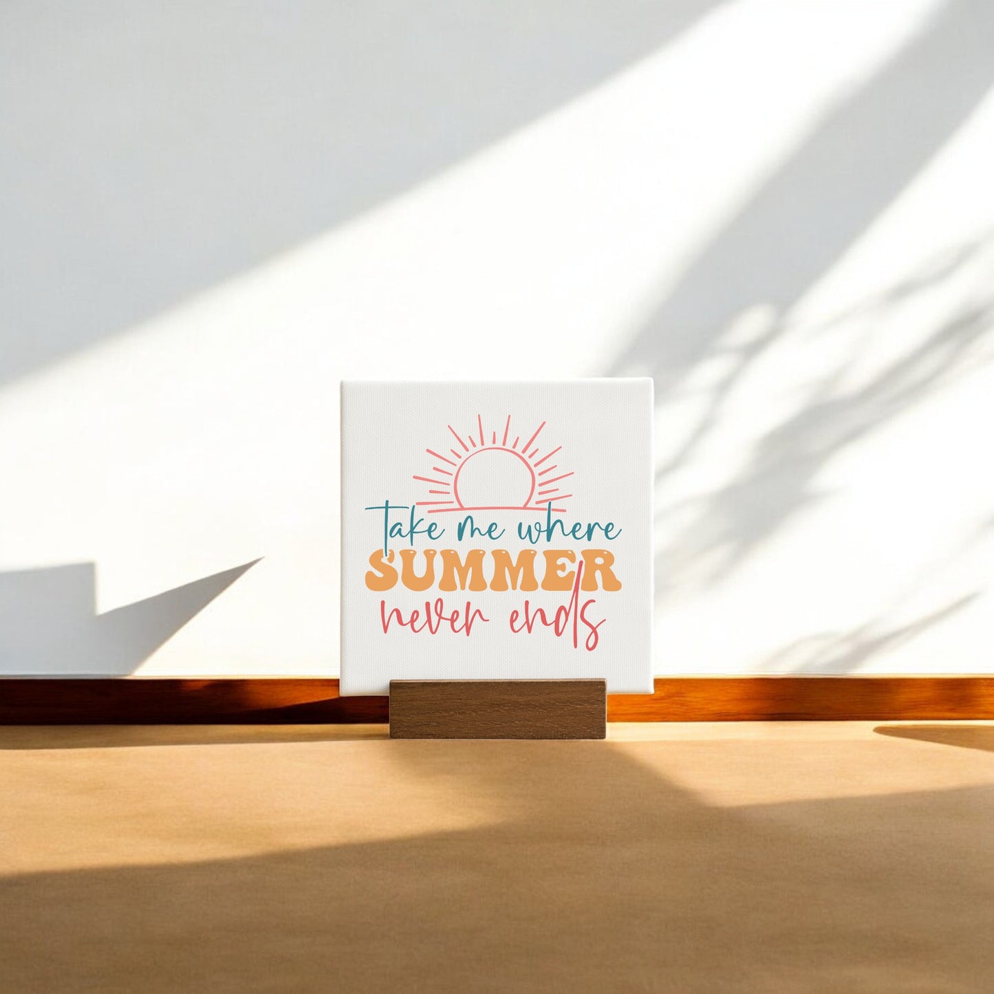 The Take Me Where Summer Never Ends Mini Canvas by Mirabilia Boutique features a sun graphic and colorful text, making it perfect for summer decor or beach house accents. Shown propped against a wall with sunlight and shadows on the floor.