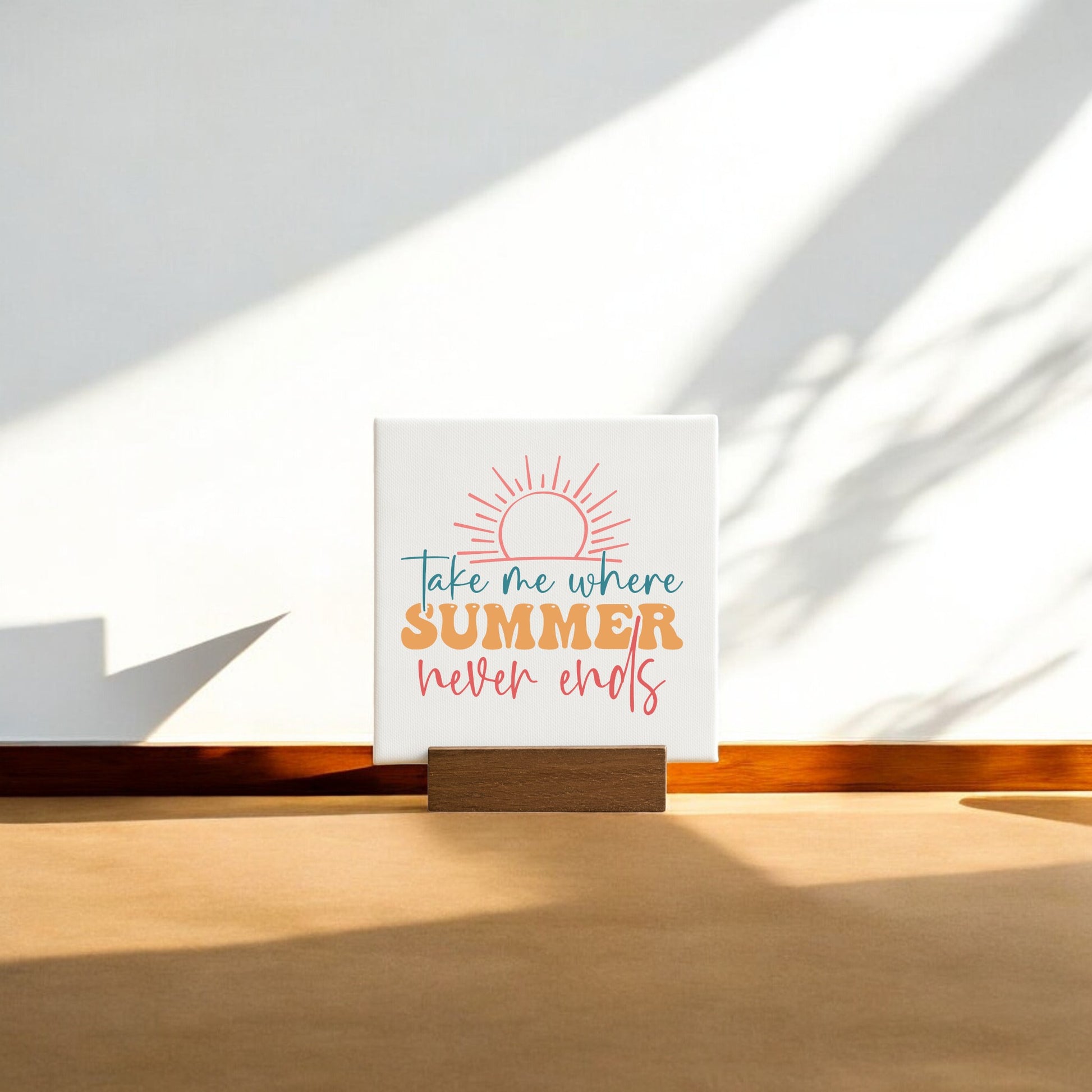 The Take Me Where Summer Never Ends Mini Canvas by Mirabilia Boutique features a sun graphic and colorful text, making it perfect for summer decor or beach house accents. Shown propped against a wall with sunlight and shadows on the floor.