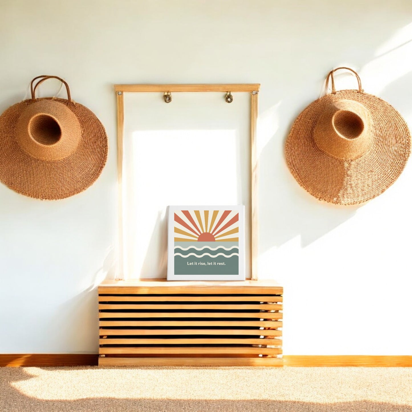 A minimalist entryway showcases two large woven hats on a wooden frame, a slatted bench below, and Mirabilia Boutique’s Let It Rise, Let It Rest Canvas – Sunrise Mindful Art. Sunlight fills the space.