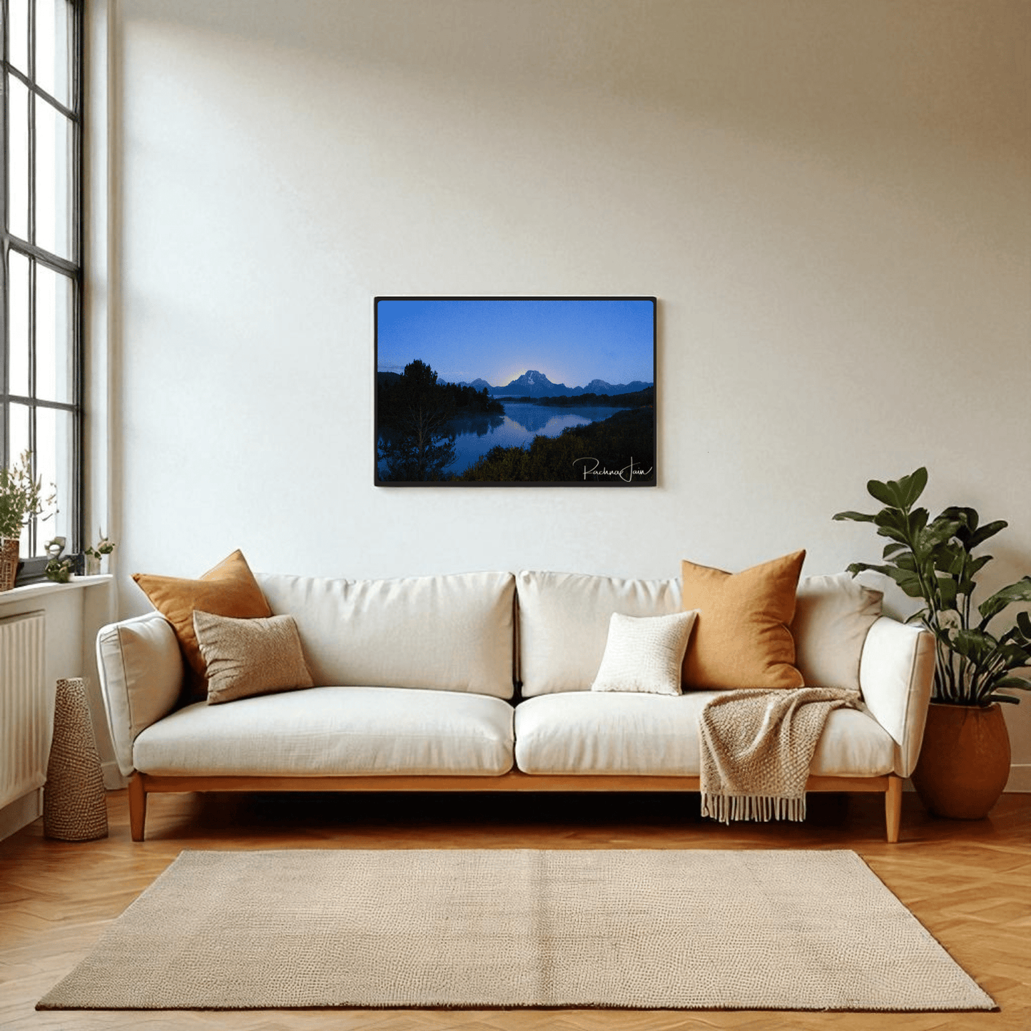 A bright living room with a cream sofa, earth-toned pillows, plants, and Sunrise at Oxbow Bend | Framed Grand Teton Art Print by Rachna Jain from Mirabilia Boutique above the couch. Sunlight pours in through large windows.