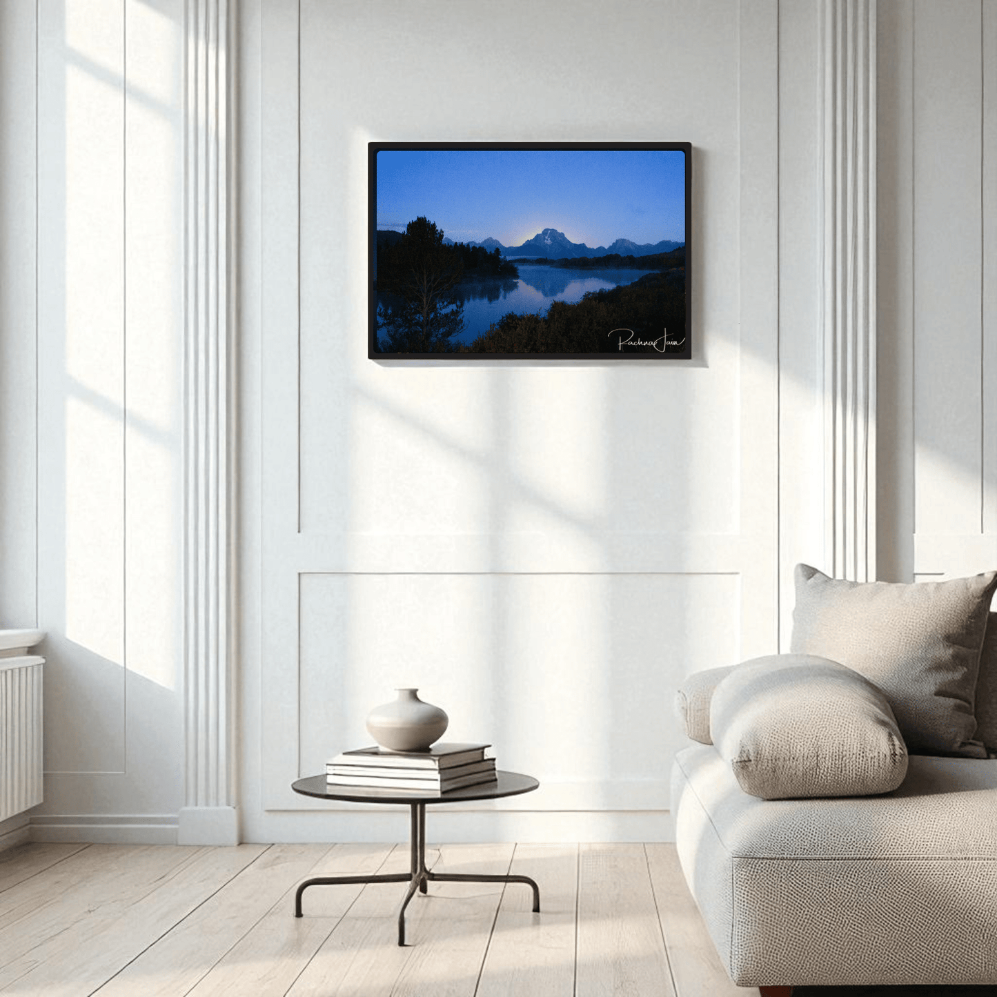Modern living room with a light gray sofa, round coffee table, and Sunrise at Oxbow Bend | Framed Grand Teton Art Print by Rachna Jain from Mirabilia Boutique displayed on a white paneled wall.