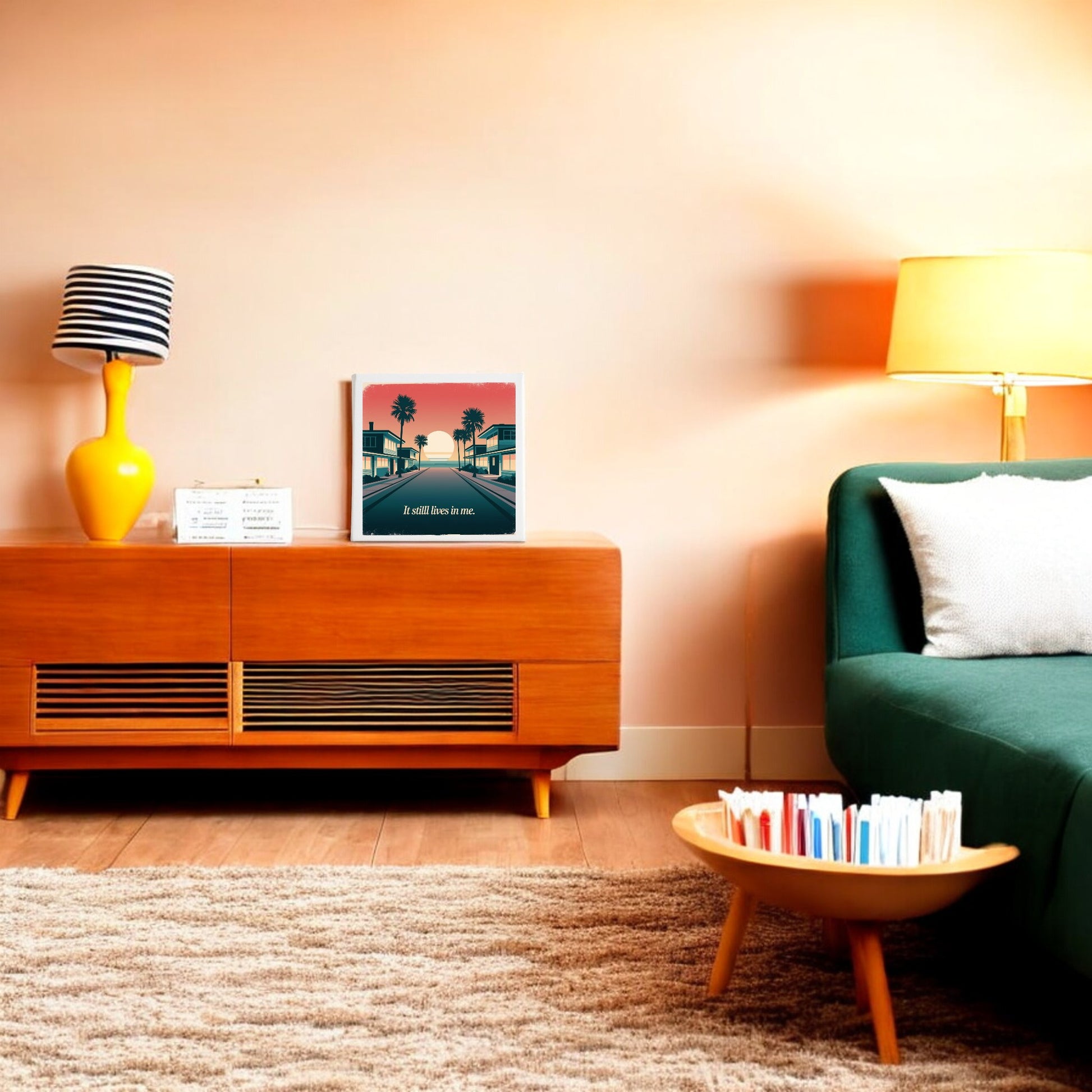 A cozy living room features a green sofa, wooden side table with books, and a console with decor. Retro beach touches and Mirabilia Boutique's "It Still Lives in Me Canvas – Retro Sunset Memory Art" add charm to the peach wall, softly lit by a floor lamp.