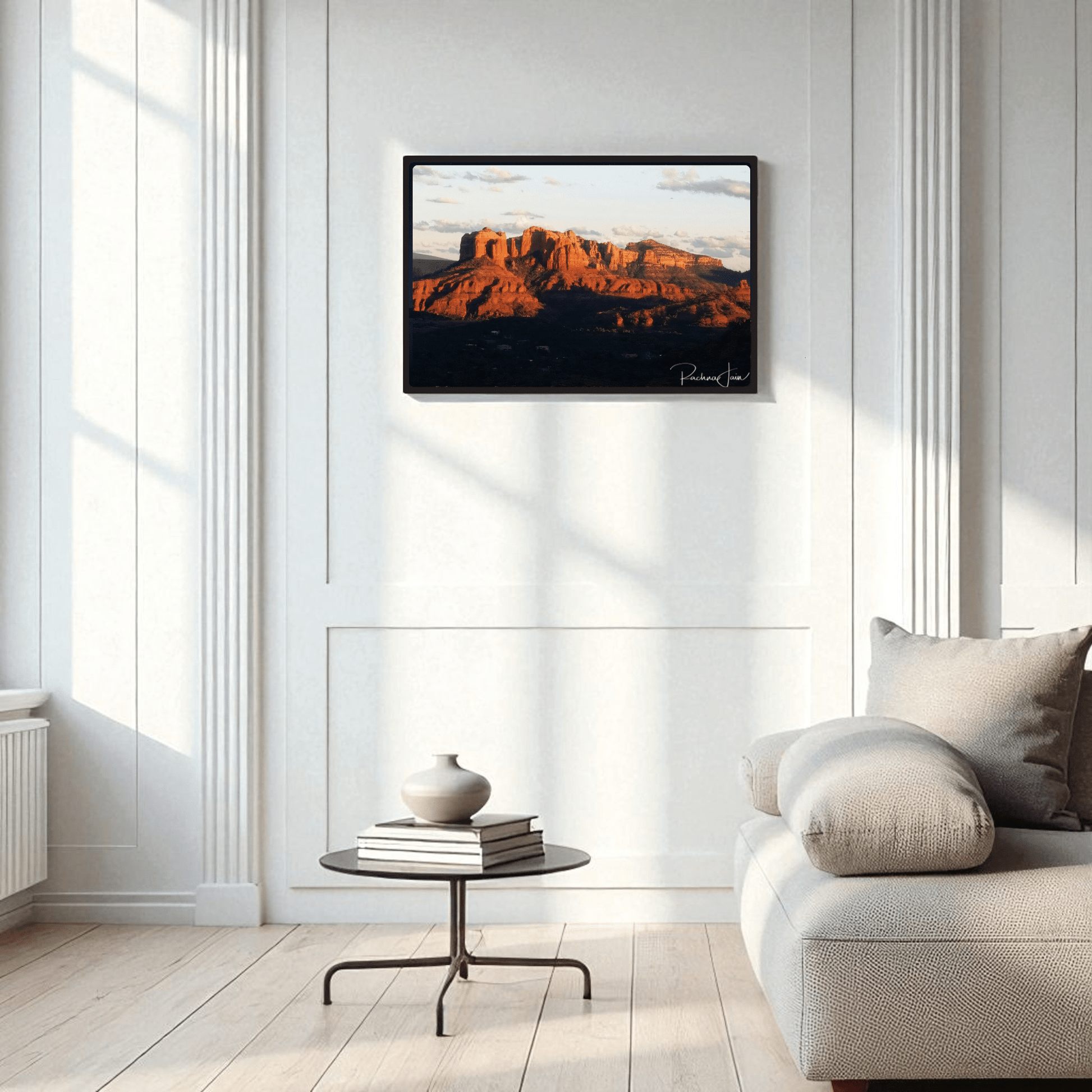 The Sunset in Sedona framed art print by Rachna Jain from Mirabilia Boutique hangs above a modern round table with vases, beside a light sofa in an elegant, bright living room with tall panels and large windows.