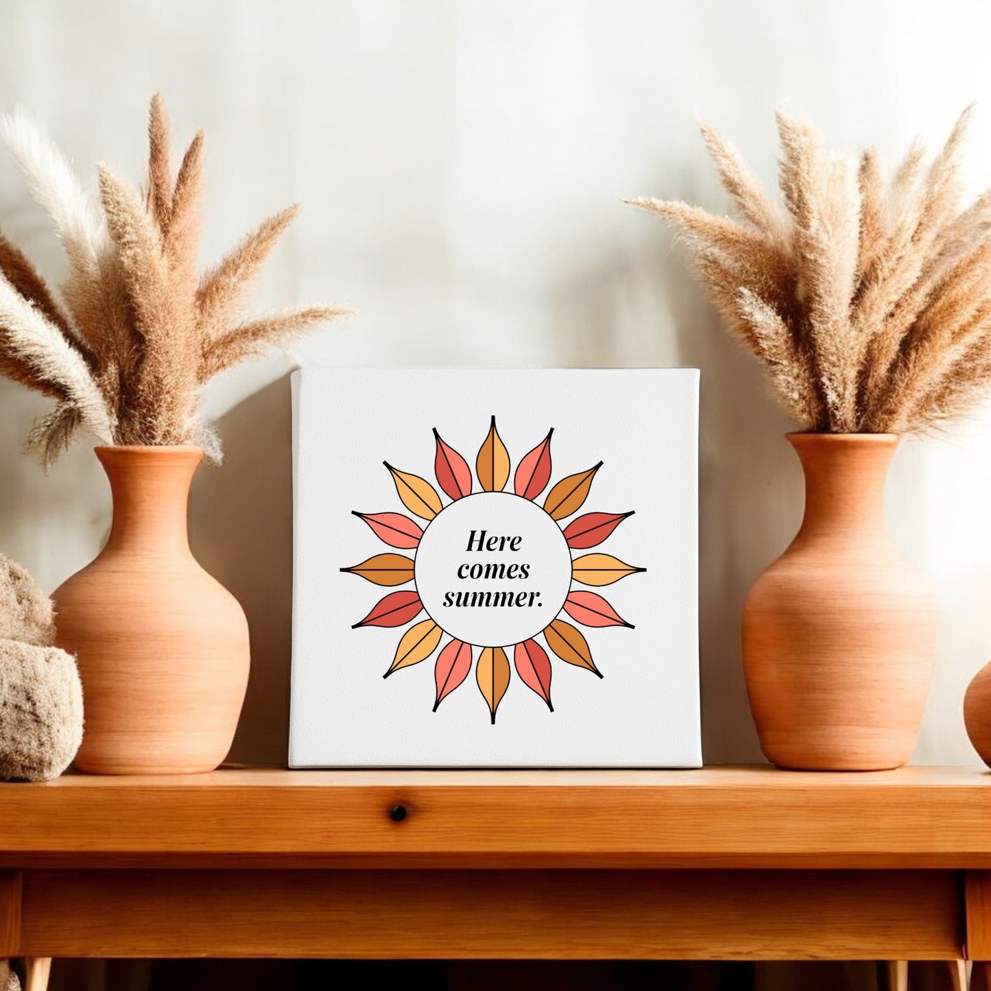 The Here Comes Summer Canvas – Retro Sunburst Wall Art by Mirabilia Boutique features a sunburst and the phrase "Here comes summer," displayed on a shelf with terracotta vases and pampas grass for vibrant seasonal decor.