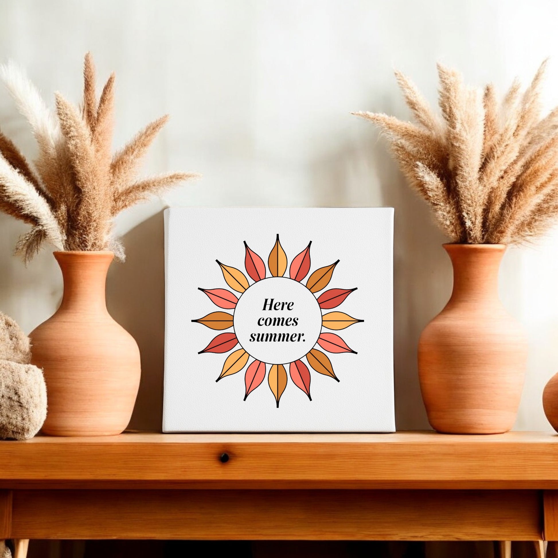 The Here Comes Summer Canvas – Retro Sunburst Wall Art by Mirabilia Boutique features a sunburst and the phrase "Here comes summer," displayed on a shelf with terracotta vases and pampas grass for vibrant seasonal decor.