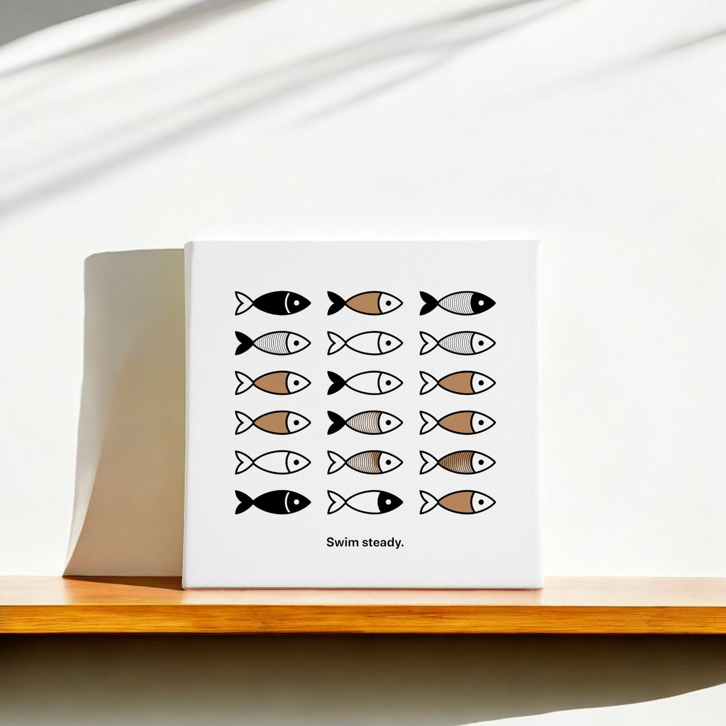 The Swim Steady Canvas – Minimalist Neutral Wall Art (8x8) by Mirabilia Boutique features four rows of simple black, brown, and gray fish with “Swim steady” text, displayed on a wooden shelf with sunlight softly shadowing the white wall.