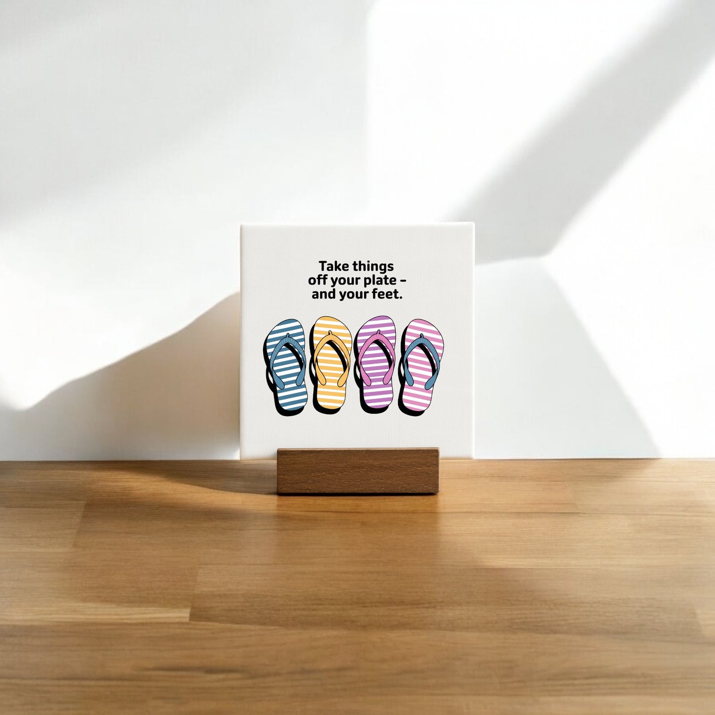 The Mirabilia Boutique "Take Things Off Your Feet" Mini Canvas (4x4) features vibrant flip-flop art and text, displayed on a wooden stand—perfect as cheerful summer decor for any sunlit space.