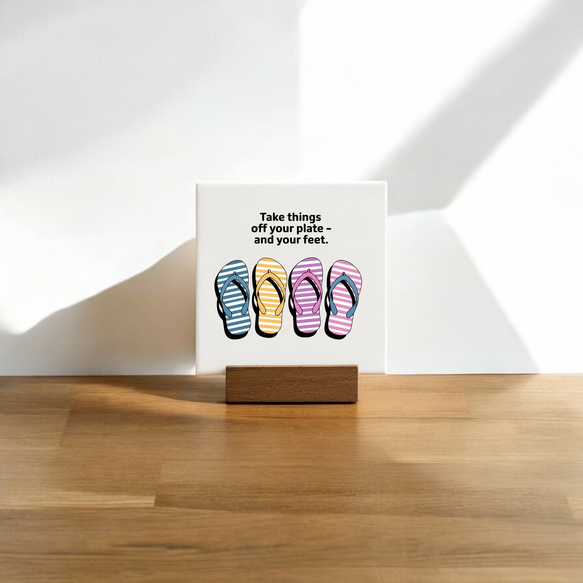 The Mirabilia Boutique "Take Things Off Your Feet" Mini Canvas (4x4) features vibrant flip-flop art and text, displayed on a wooden stand—perfect as cheerful summer decor for any sunlit space.