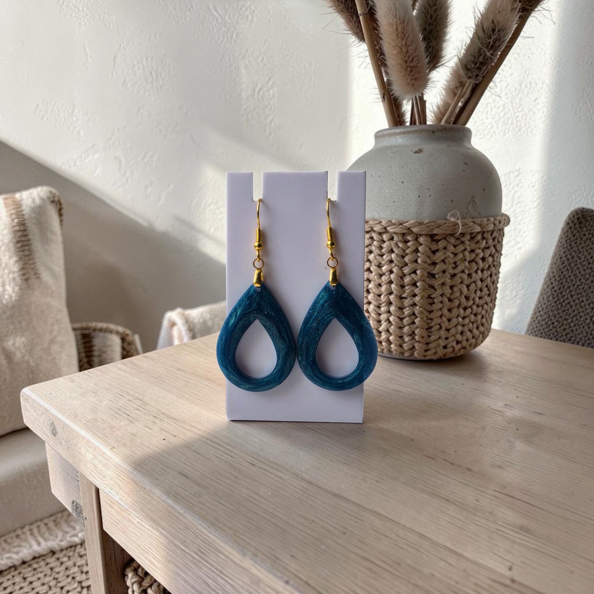 Mirabilia Boutique’s Mermaid Dust Teardrop Earrings with gold hooks are shown on a white card atop a light wooden table, accented by a woven basket and neutral decor in the background.