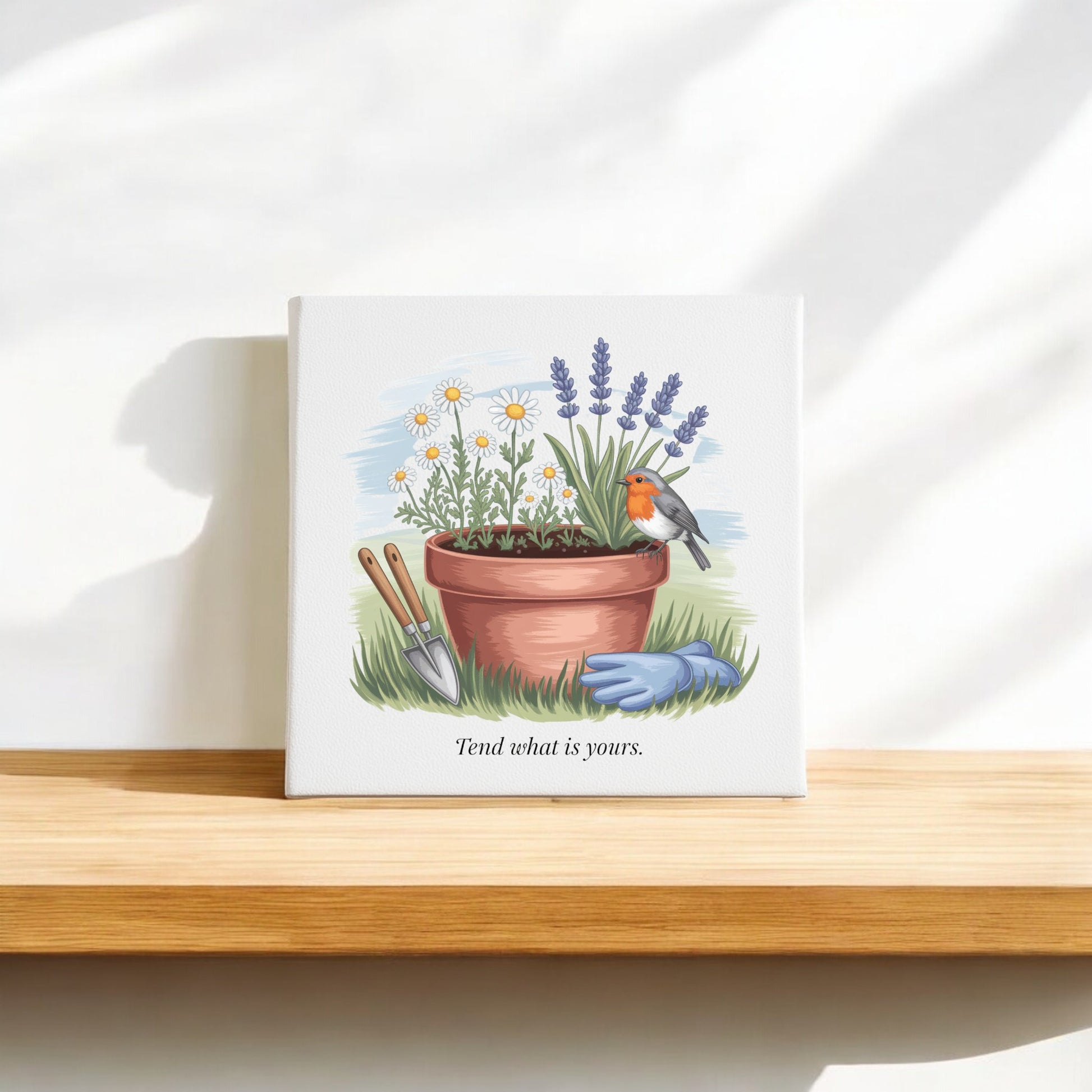 The Mirabilia Boutique “Tend What Is Yours” Canvas Sign (8x8) features daisies, lavender, a bird, and garden tools—ideal mindful home decor or gift for gardeners. Displayed on a wooden shelf with sunlight casting soft shadows.