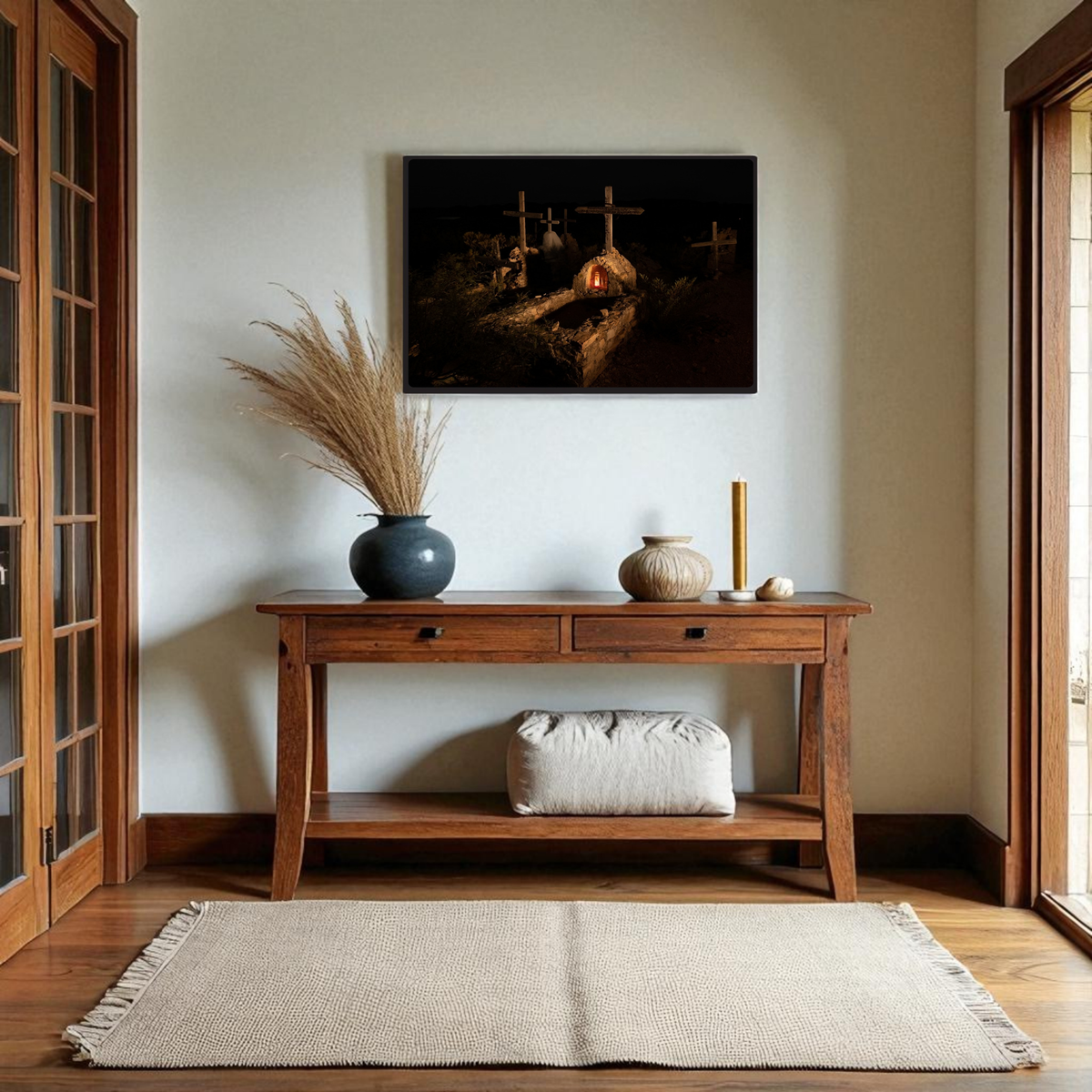 A wooden console table adorned with decorative vases stands against the wall, topped by the “Terlingua Cemetery at Night | Framed Fine Art Print” from Mirabilia Boutique, a piece inspired by West Texas photography and depicting three crosses under the night sky reminiscent of Terlingua Cemetery. A beige rug covers the wooden floor below, and a cushion rests beneath the table.