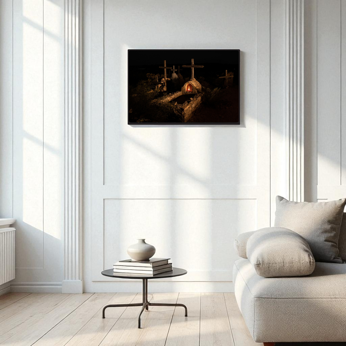 A modern, minimalist living room with white walls, a light sofa, and a round glass coffee table features the Terlingua Cemetery at Night | Framed Fine Art Print by Mirabilia Boutique—a West Texas-inspired artwork depicting three crosses in nighttime photography—elegantly displayed on the wall.