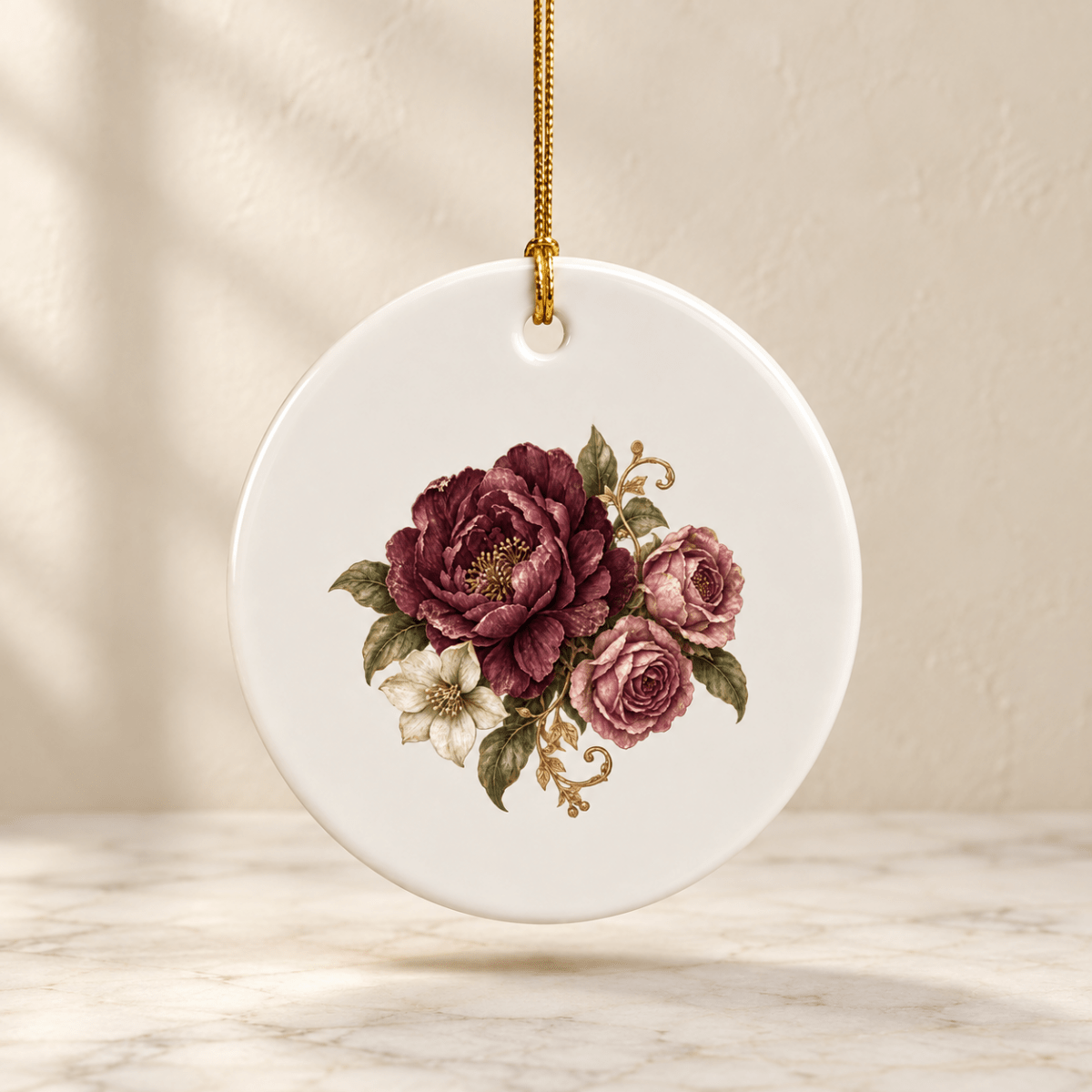 The Garden Remembered Ceramic Ornament by Mirabilia Boutique features a round white ceramic design with a gold string, beautifully adorned with hand-painted burgundy and pink roses, lush green leaves, and delicate gold accents—an elegant piece from the Velvet Ruins collection that makes an ideal gift for flower lovers.