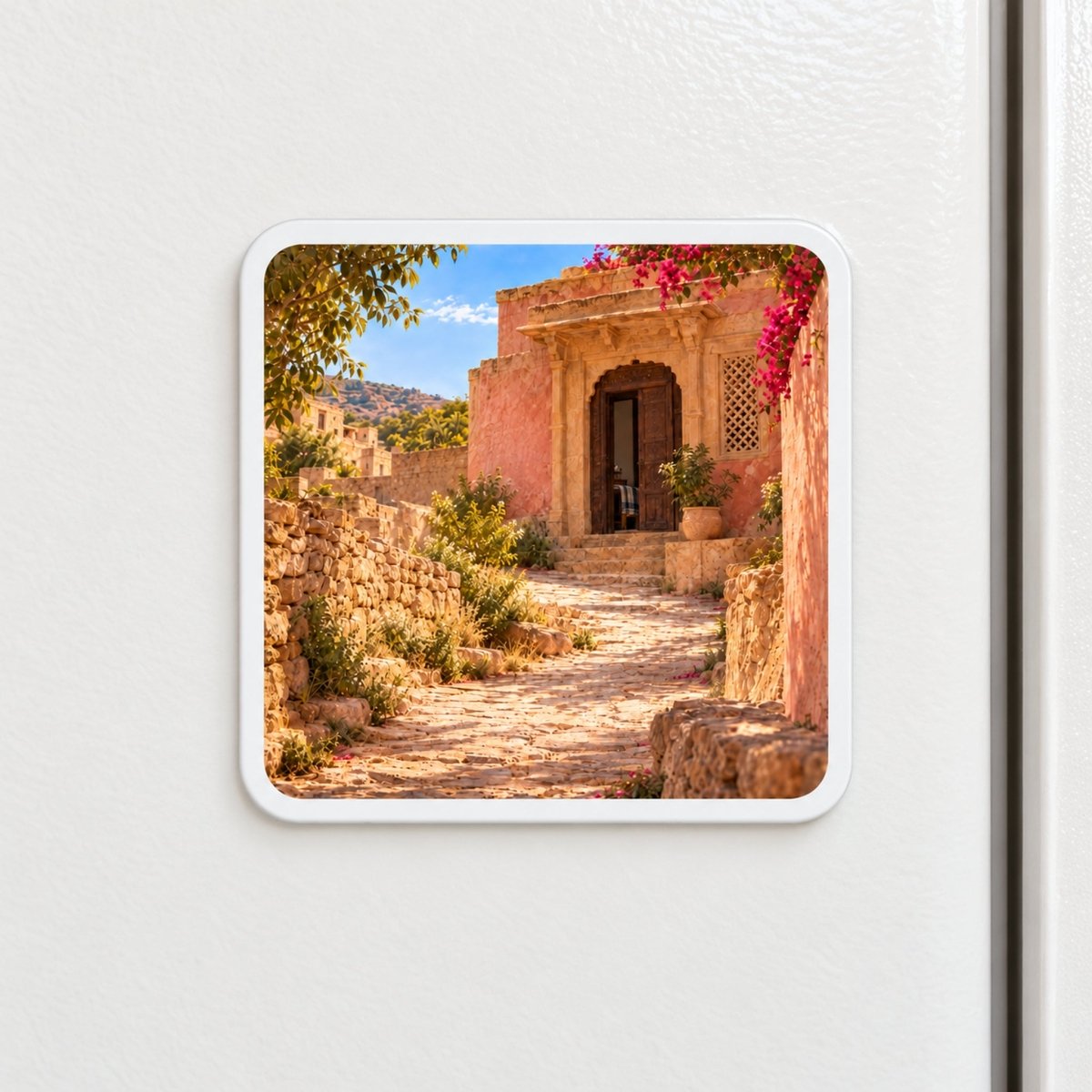 The House Ahead Magnet | Sand & Saffron is a square decorative hardboard magnet on a white surface featuring a sunlit stone path leading to a pink building with an open wooden doorway.