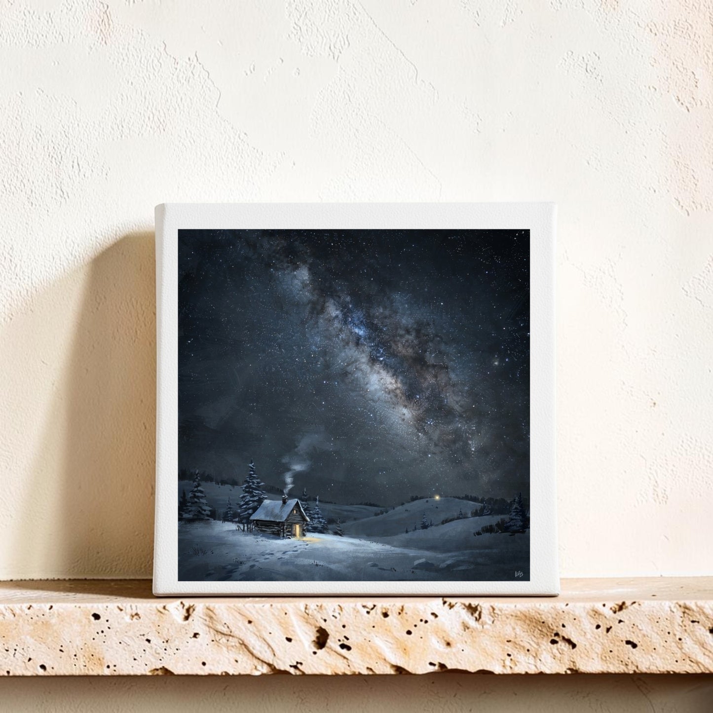 An 8x8 “The Night Is Listening Milky Way Canvas Art” by Mirabilia Boutique, depicting a snowy cabin beneath a star-filled sky and the glowing Milky Way, is displayed on a stone shelf against a textured cream wall.