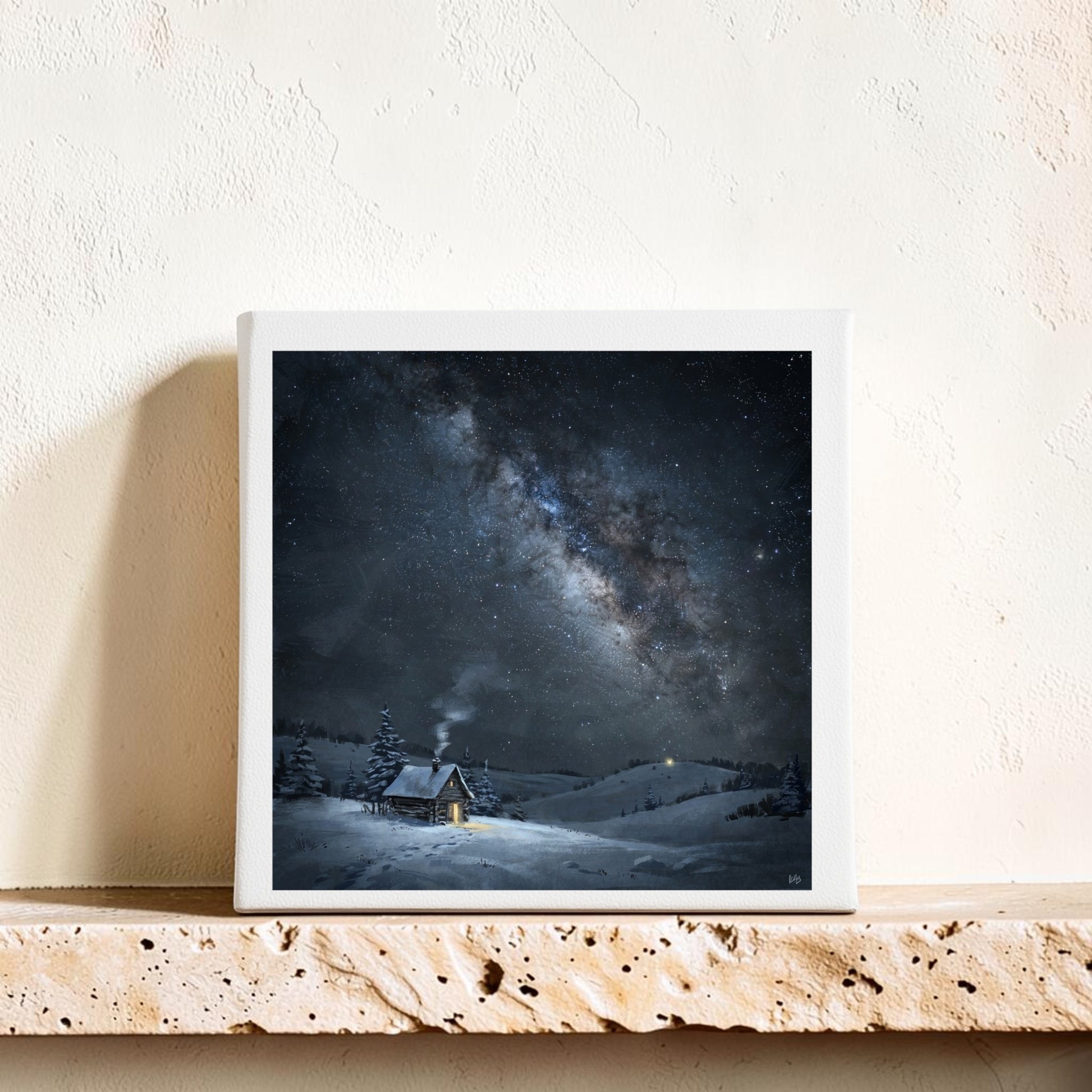 An 8x8 “The Night Is Listening Milky Way Canvas Art” by Mirabilia Boutique, depicting a snowy cabin beneath a star-filled sky and the glowing Milky Way, is displayed on a stone shelf against a textured cream wall.